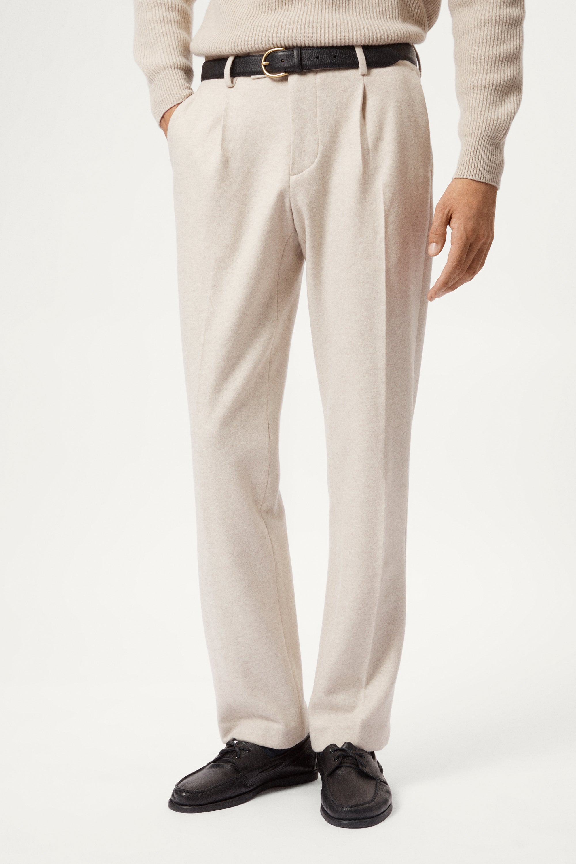 Person wearing a woolen beige pants and a light sweater on a white background