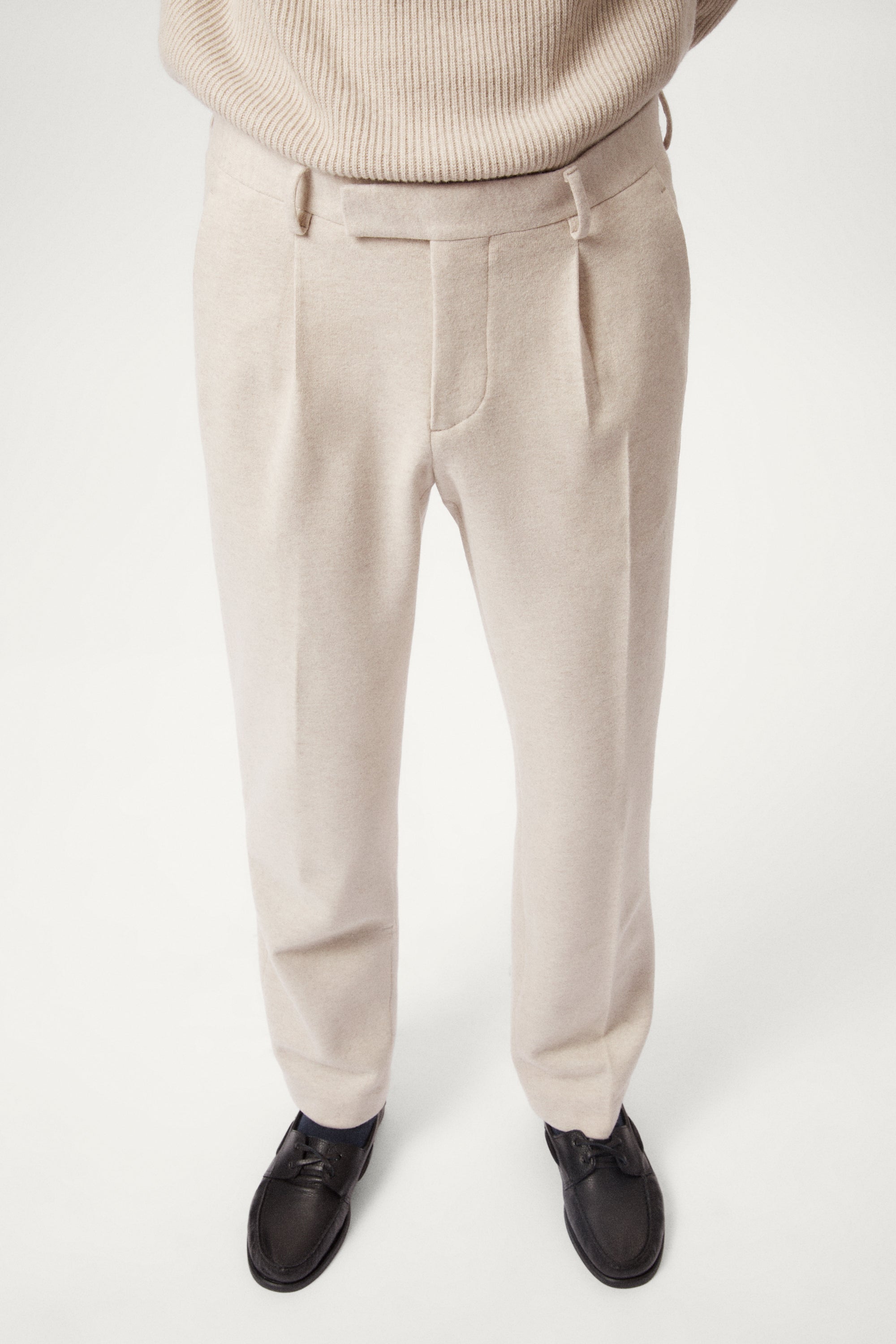 Person wearing a woolen beige pants and a light sweater on a white background
