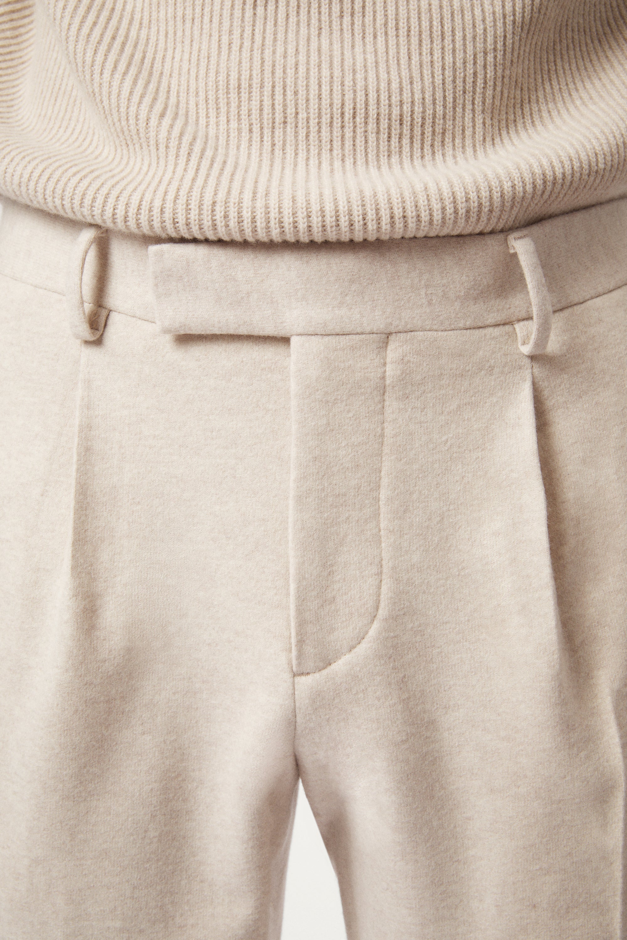 Close-up of beige pants and sweater on a neutral background
