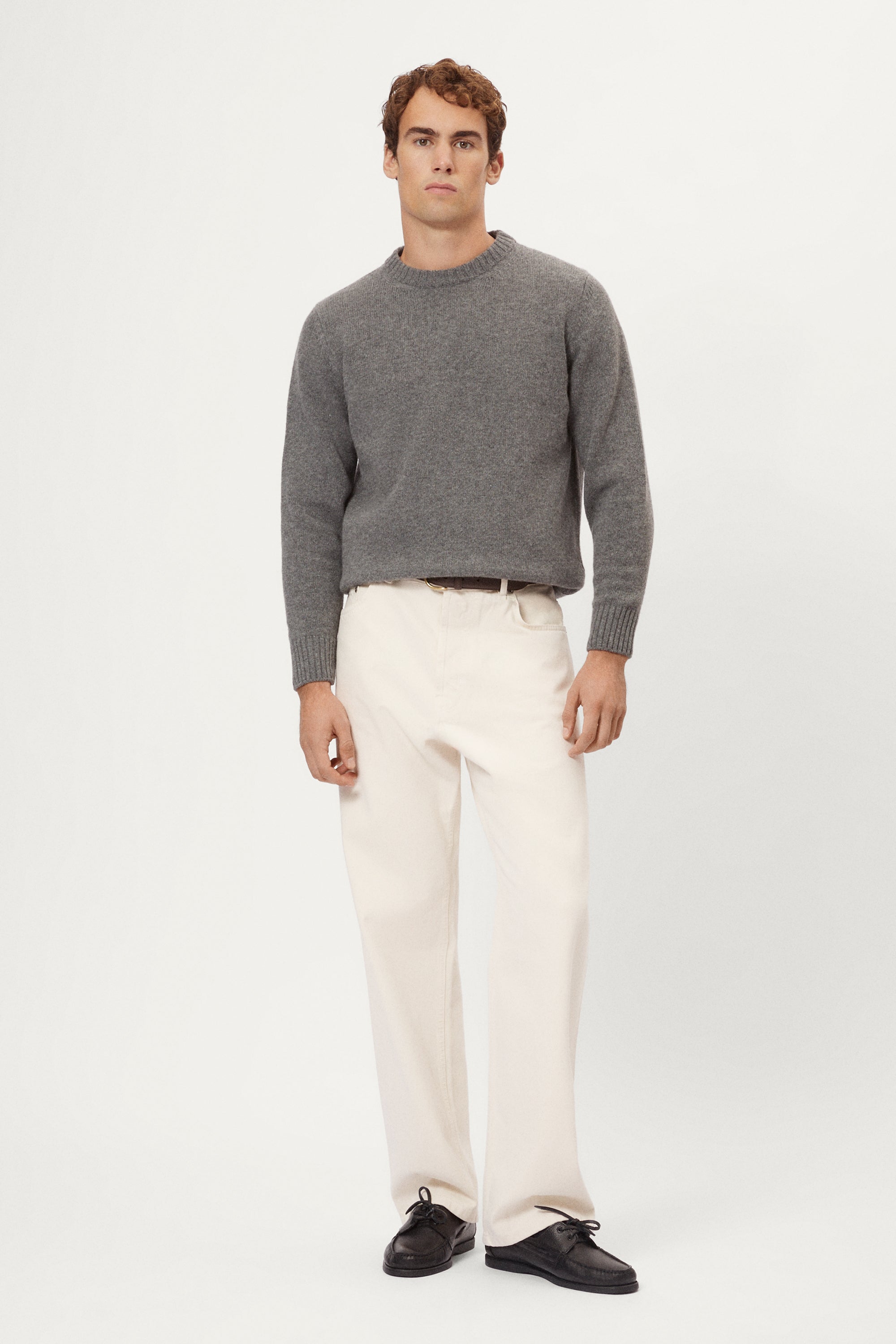 Man wearing a gray woolen sweater and white pants against a white background