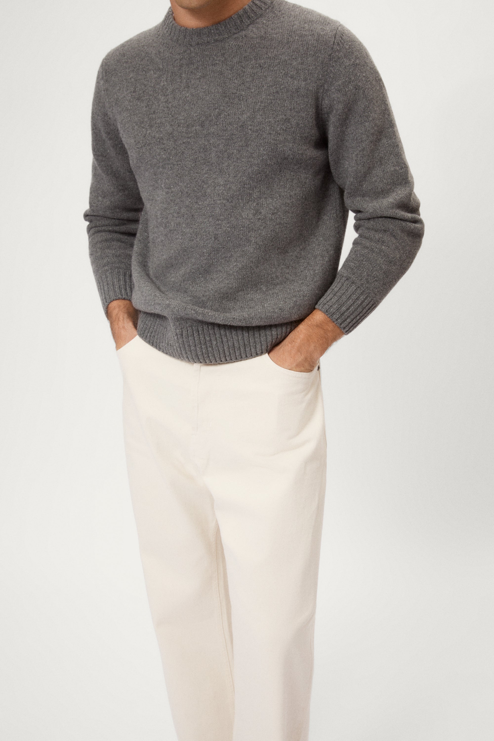 Man wearing a gray woolen sweater and white pants against a white background