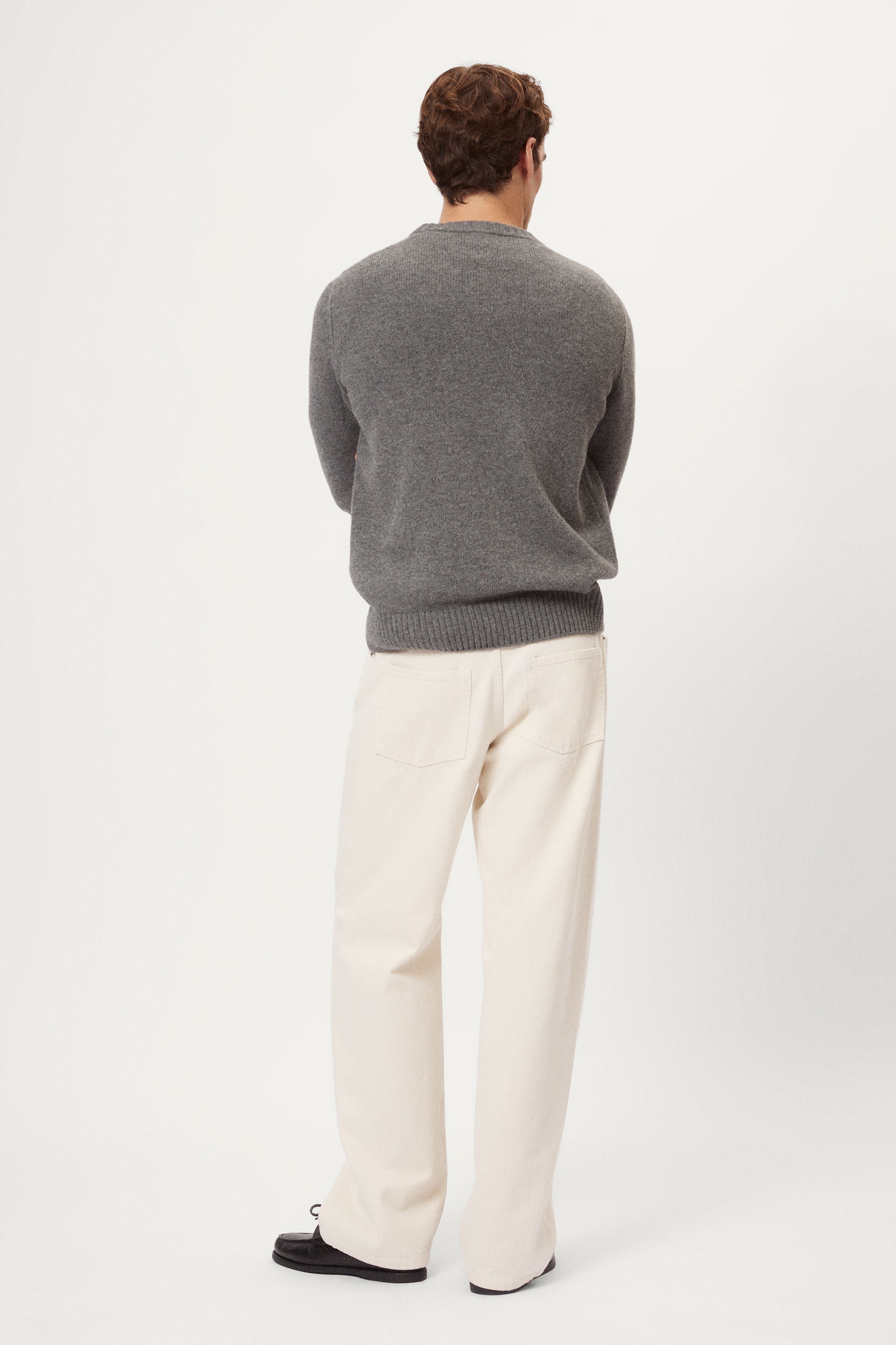 Man wearing a gray woolen sweater and white pants against a white background