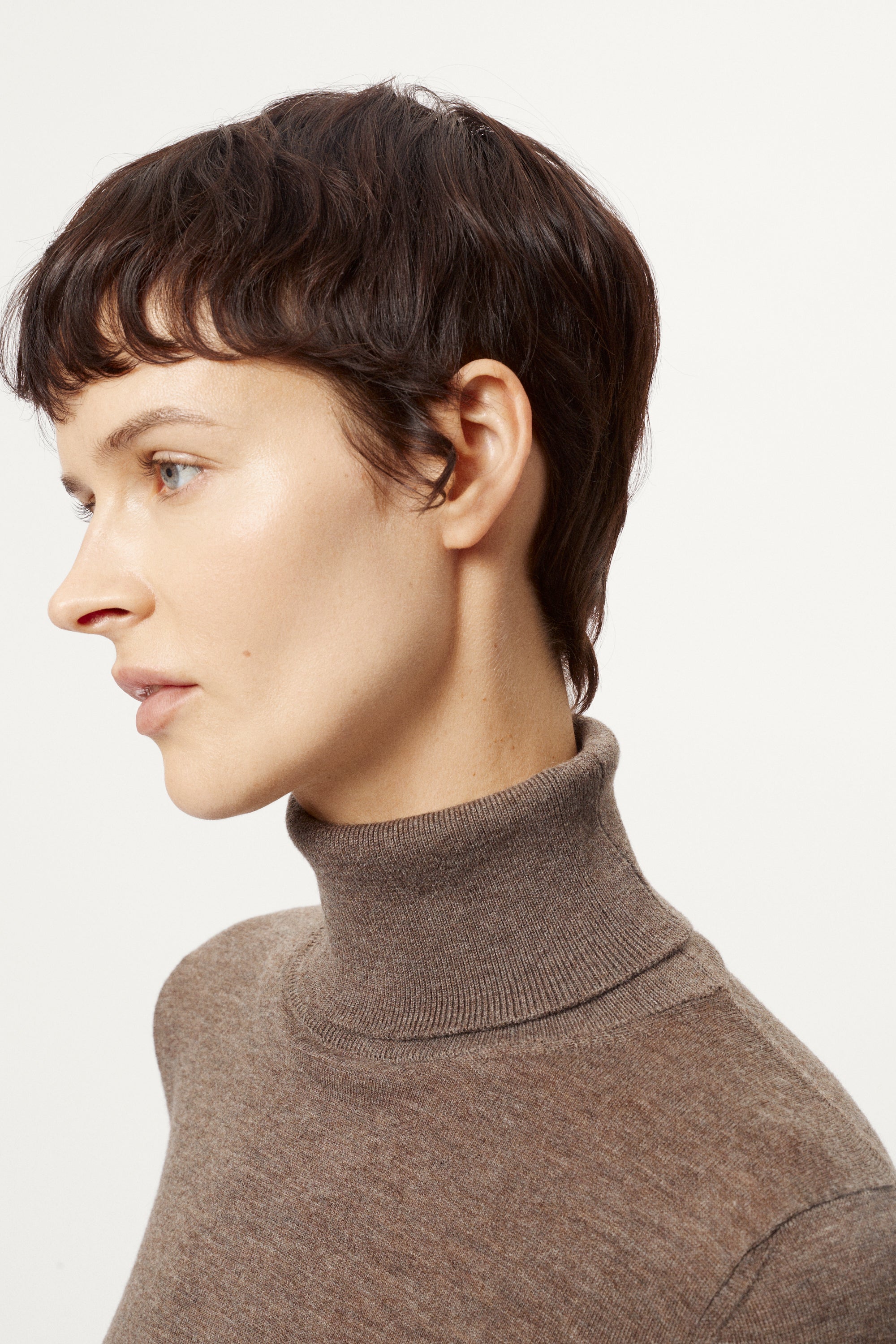 Woman wearing a brown turtleneck sweater against a white background