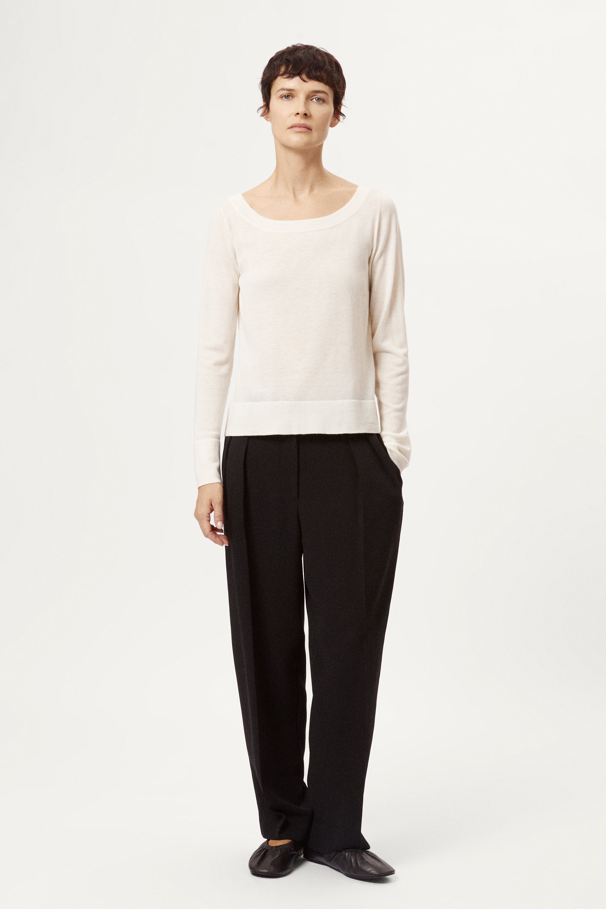 Person wearing a white sweater and black pants on a white background