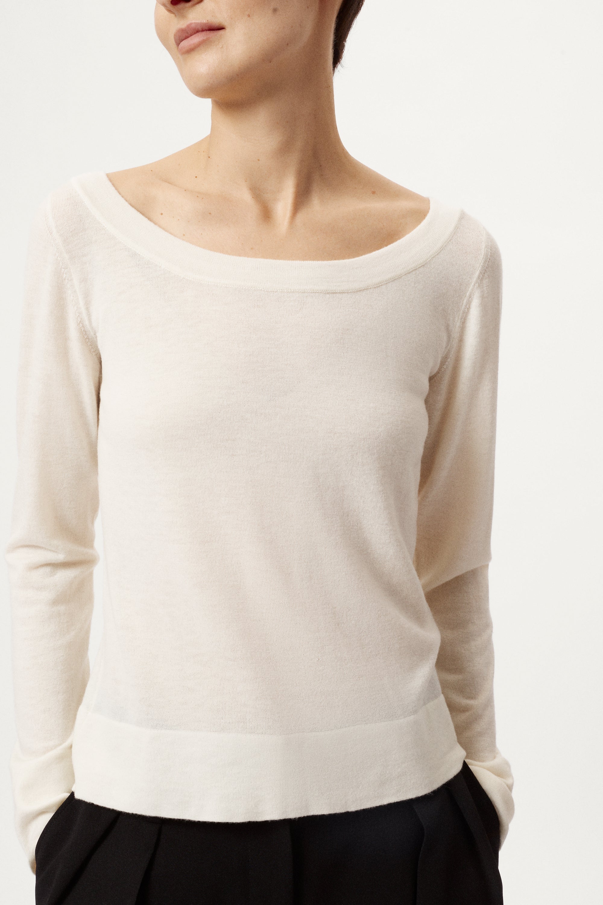 Person wearing a beige long-sleeve top with a plain background