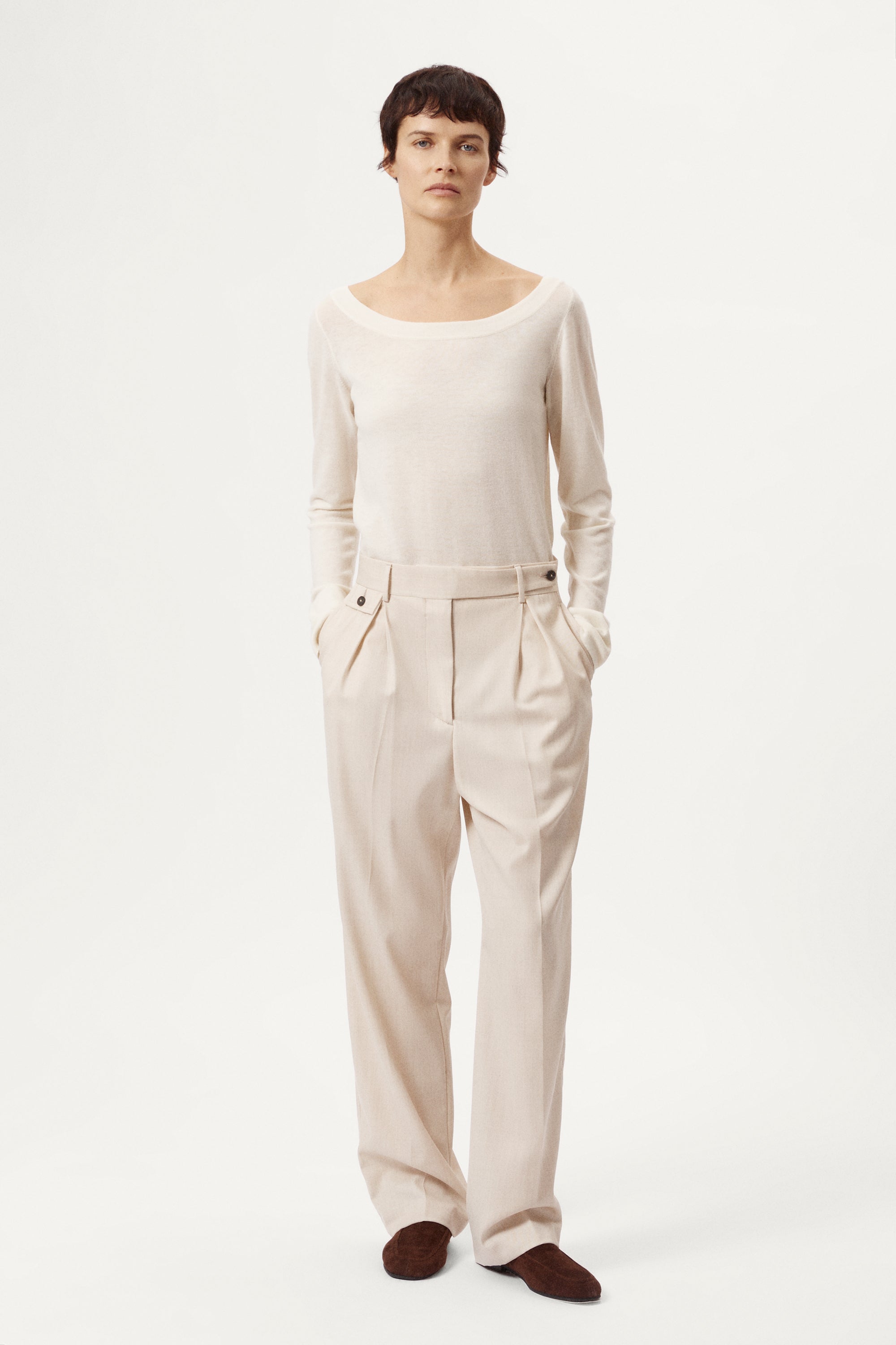 Person wearing a white sweater and black pants on a white background