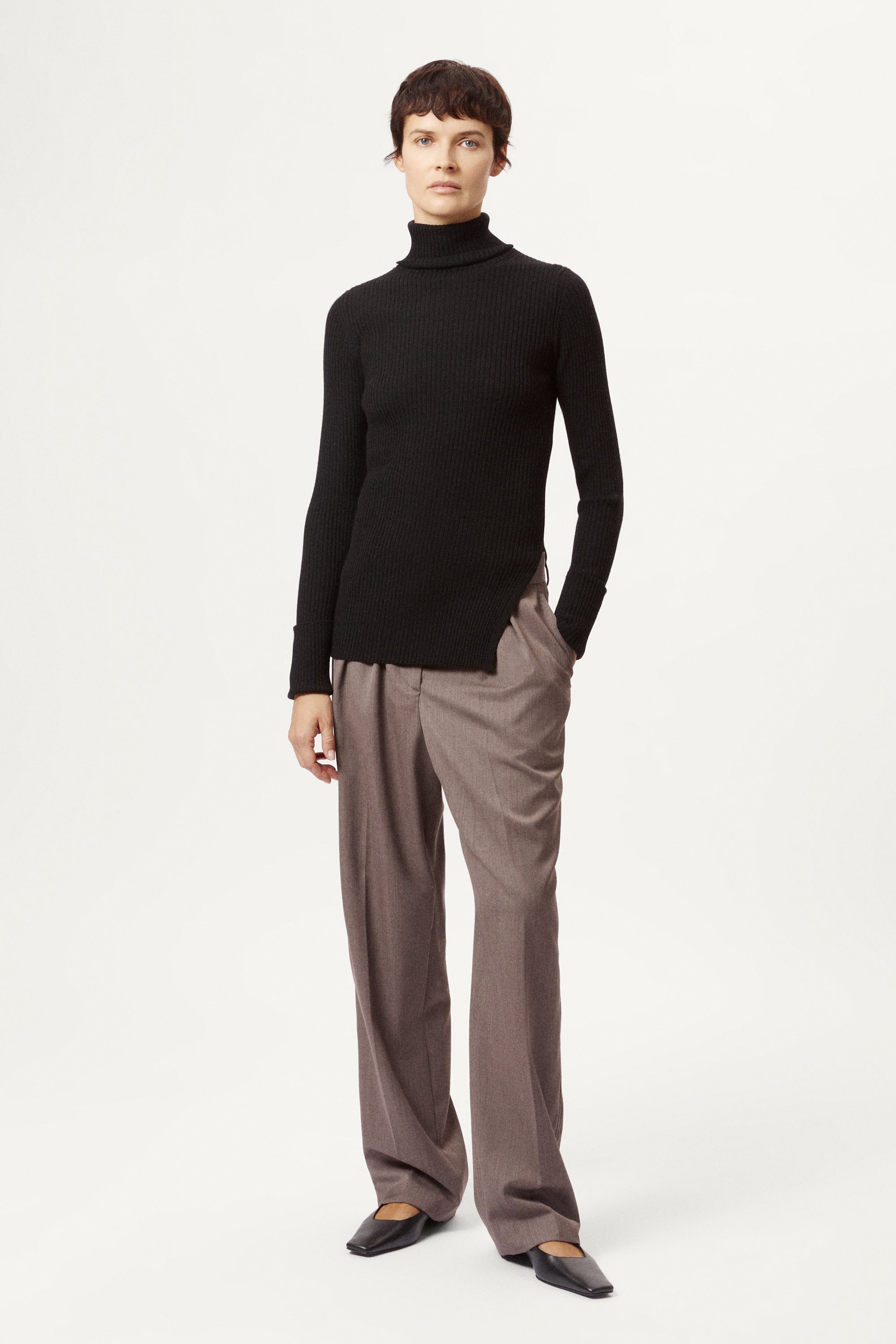 Person wearing a black turtleneck and gray pants on a white background