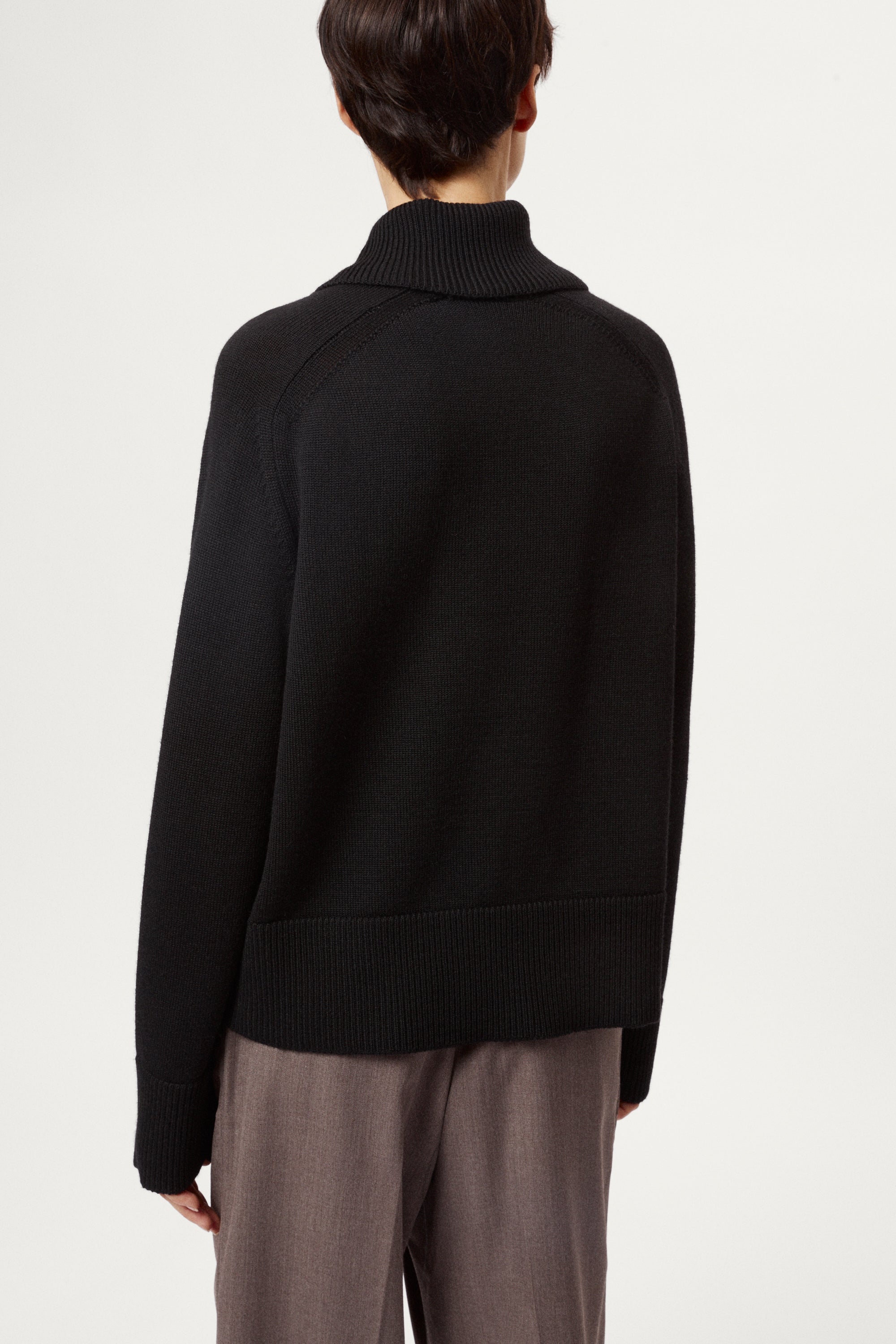 Person wearing a black sweater and gray pants on a white background