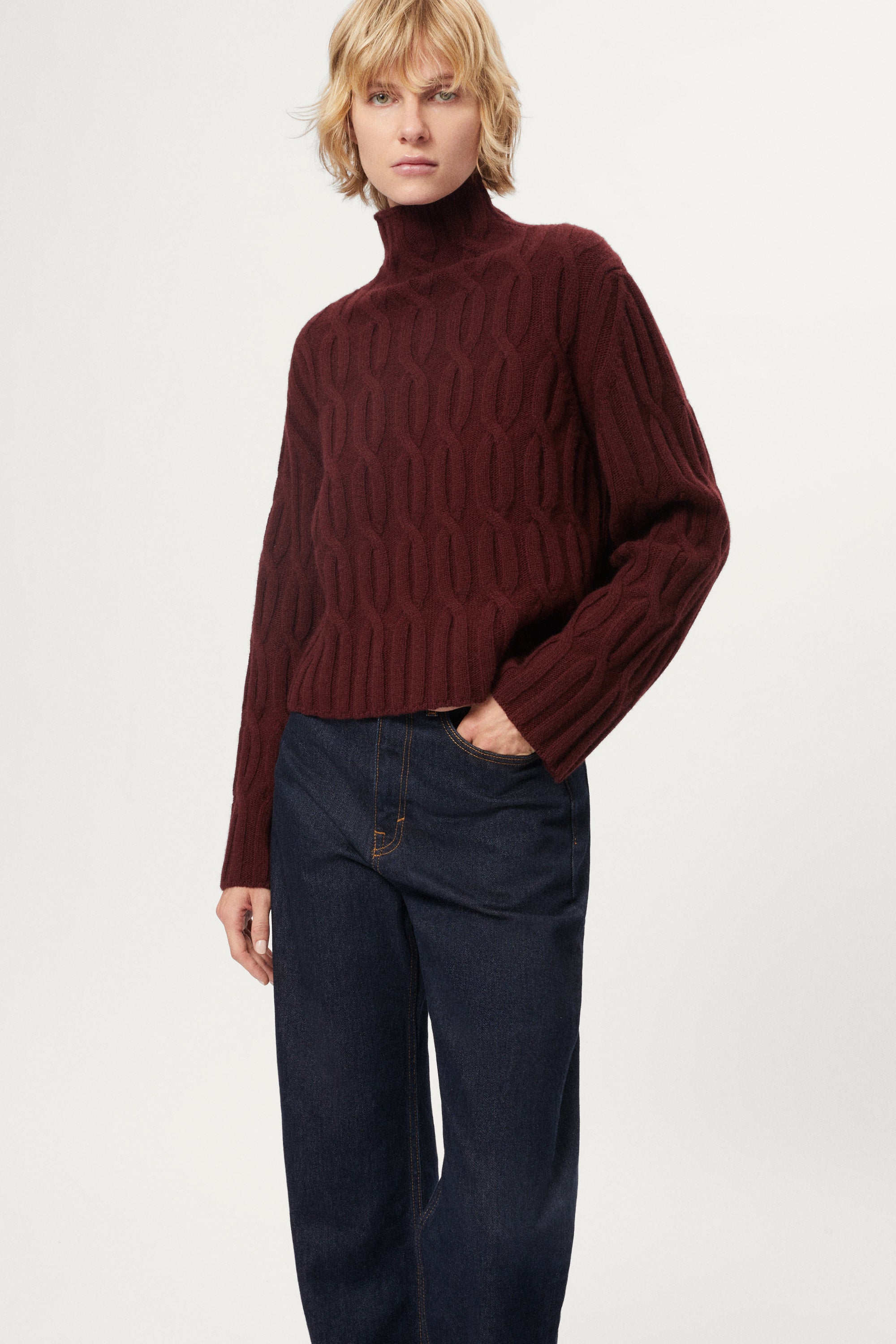 woman wearing a burgundy turtleneck sweater and dark pants on a white background