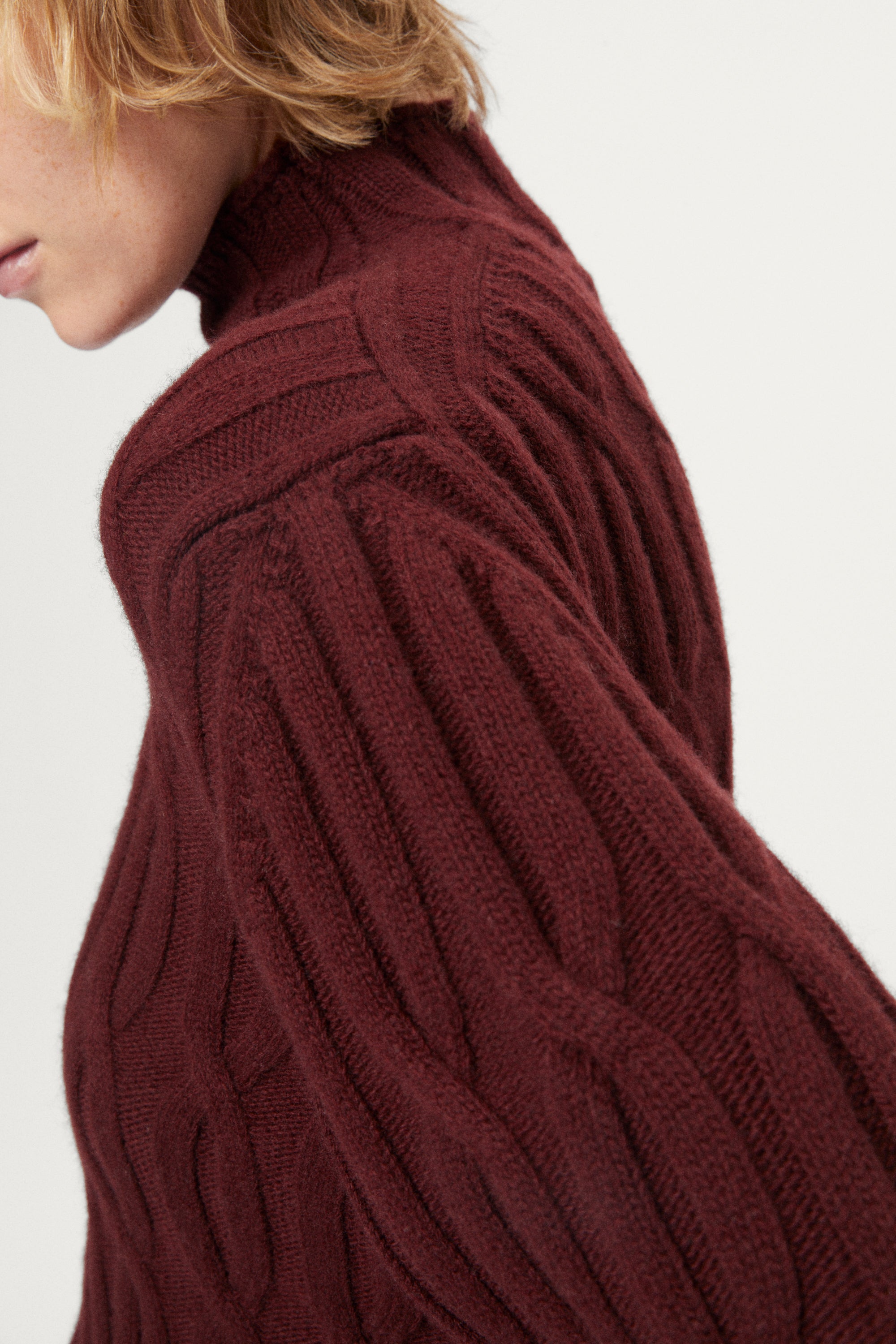 woman wearing a burgundy turtleneck sweater and dark pants on a white background