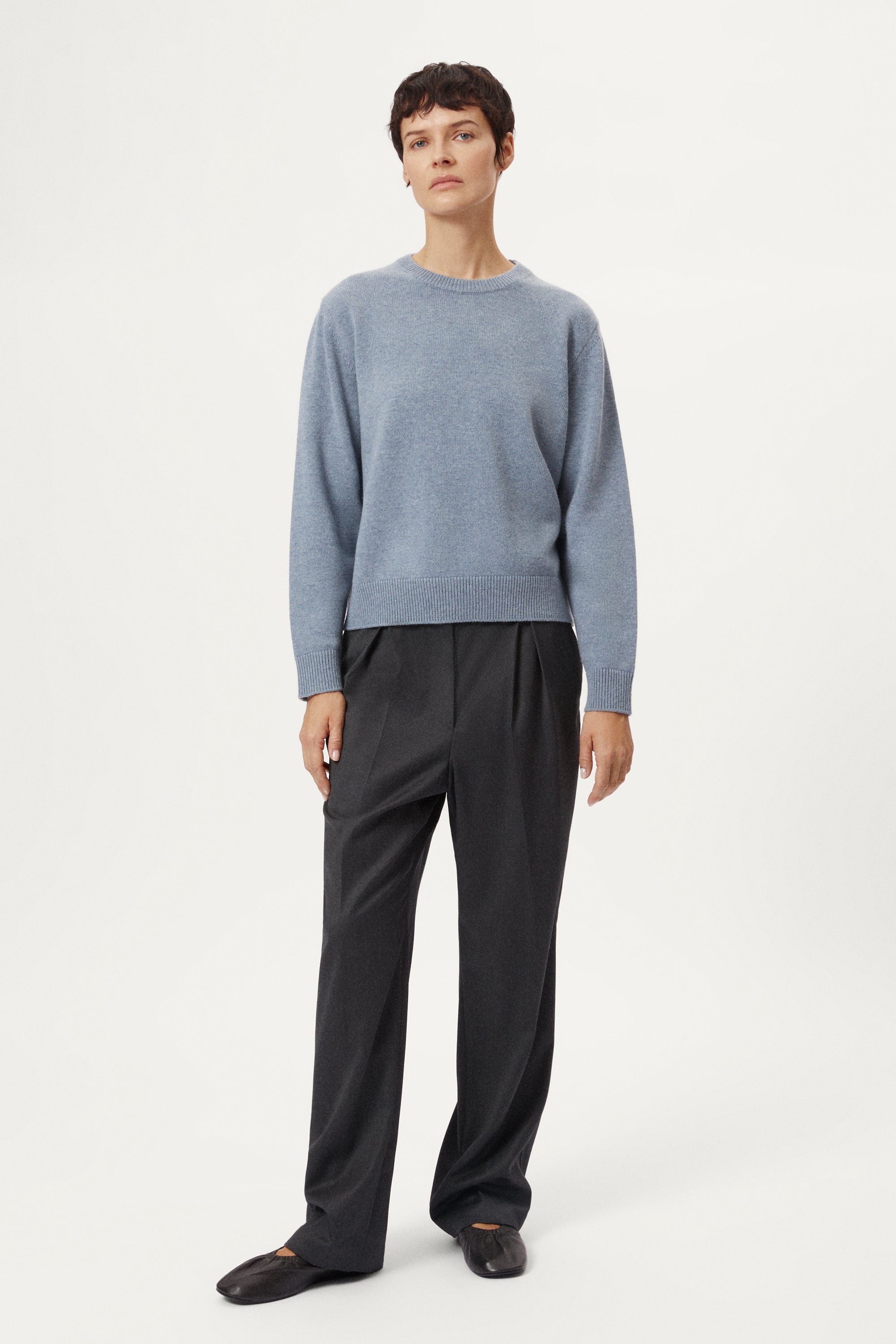 woman wearing a woolen light blue sweater and dark pants on a white background