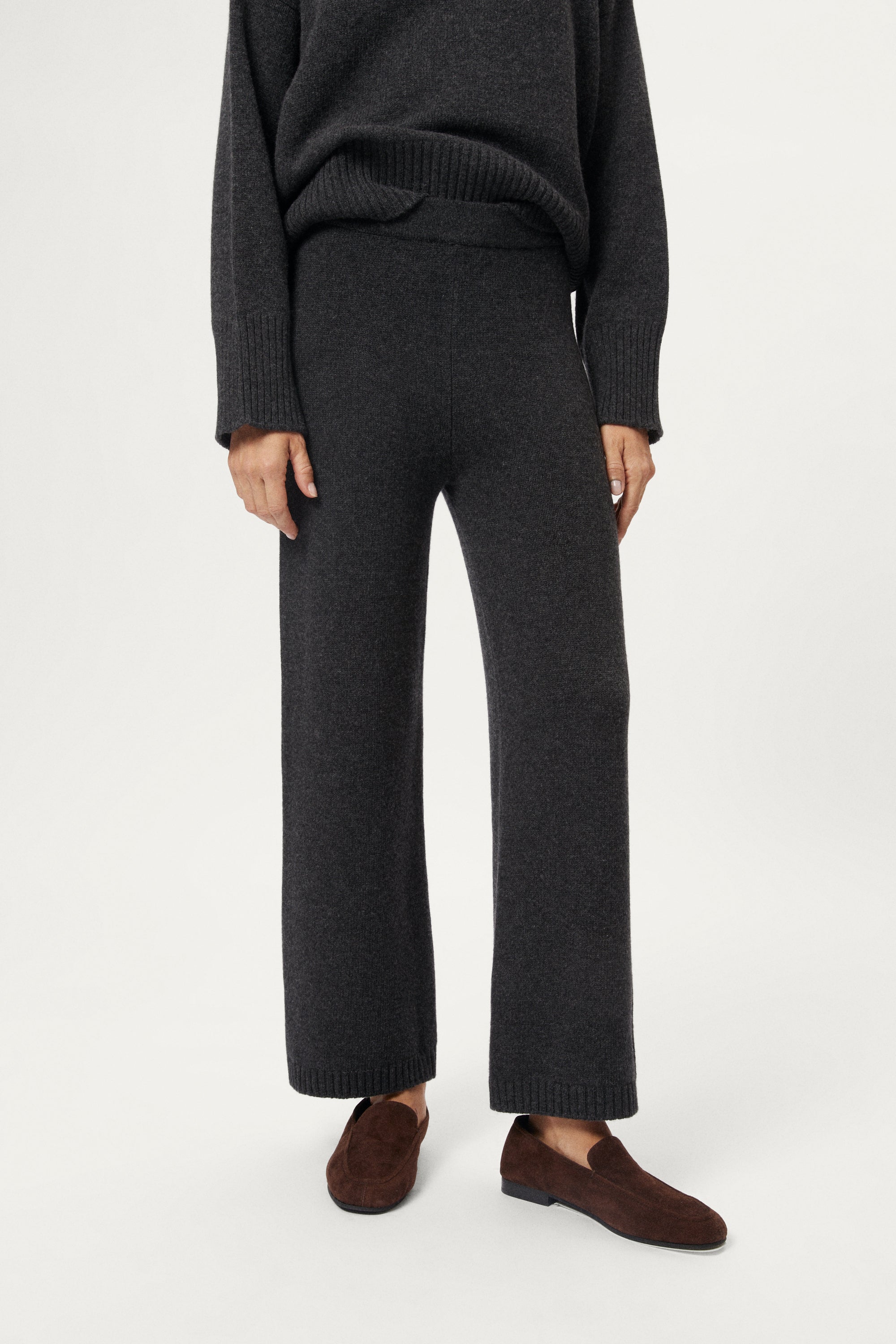Woman wearing a woolen dark gray sweater and pants with brown shoes on a white background