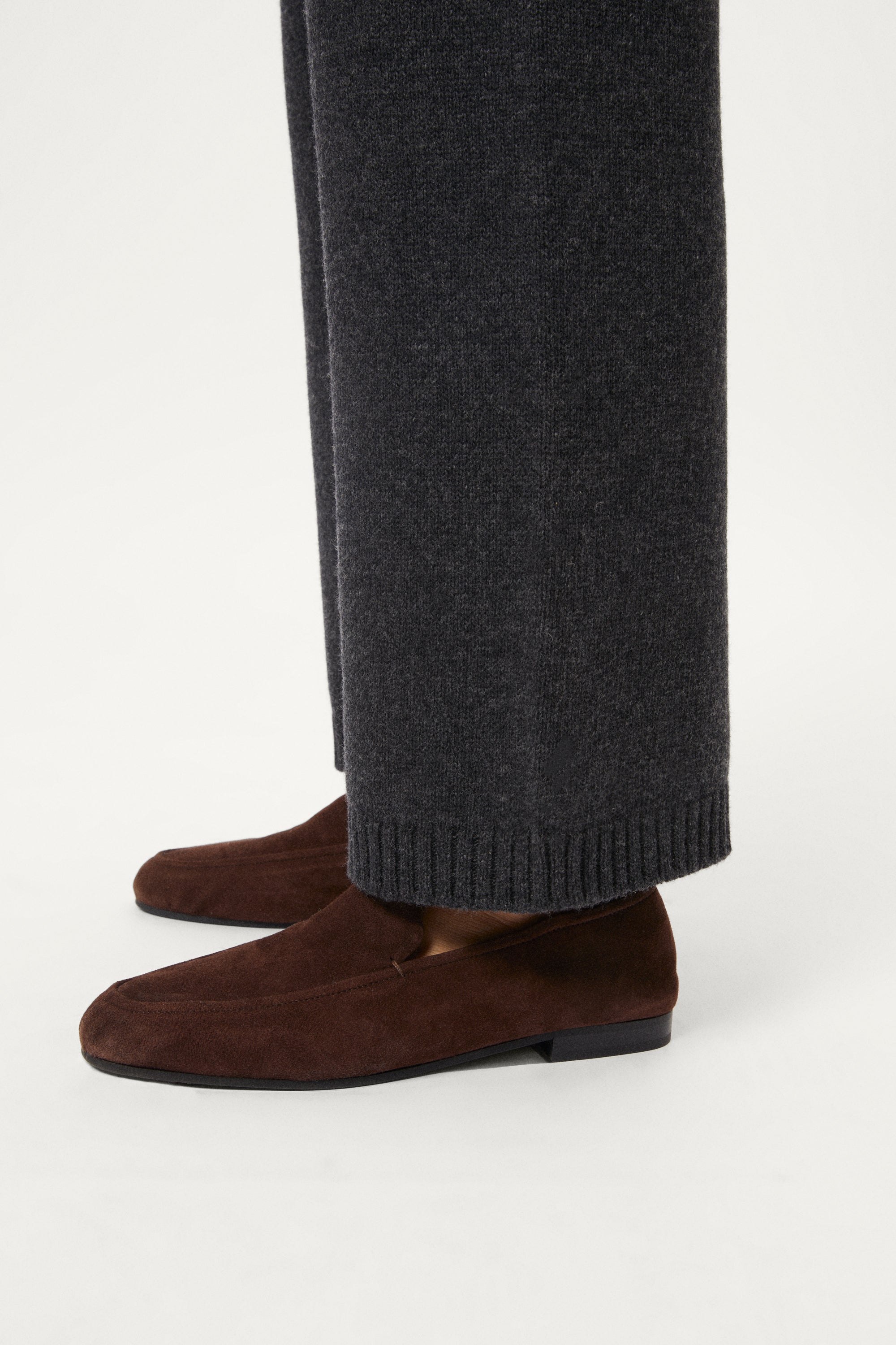 Woman wearing a woolen dark gray pants with brown shoes on a white background