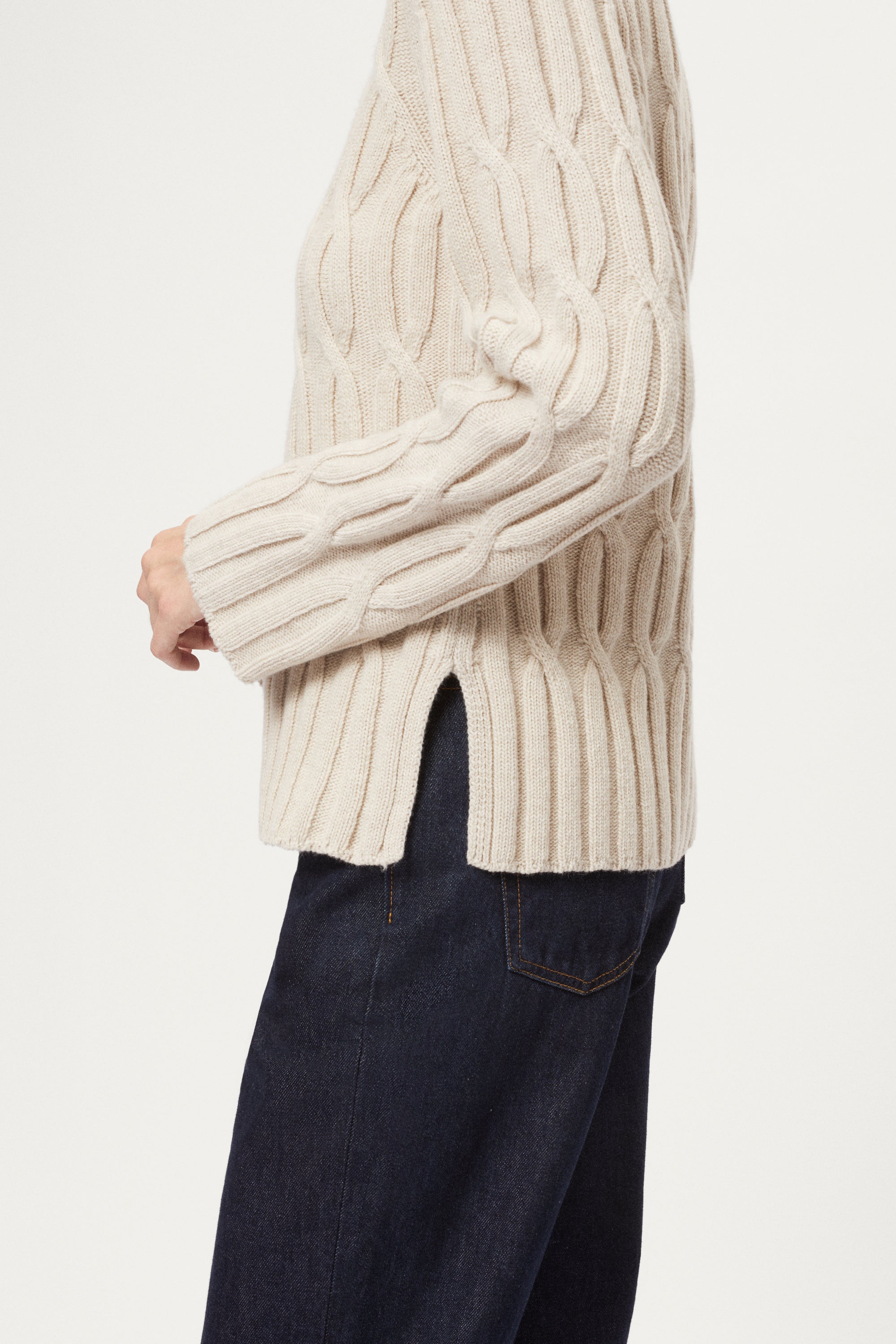 Beige cable knit sweater worn by a person on a white background