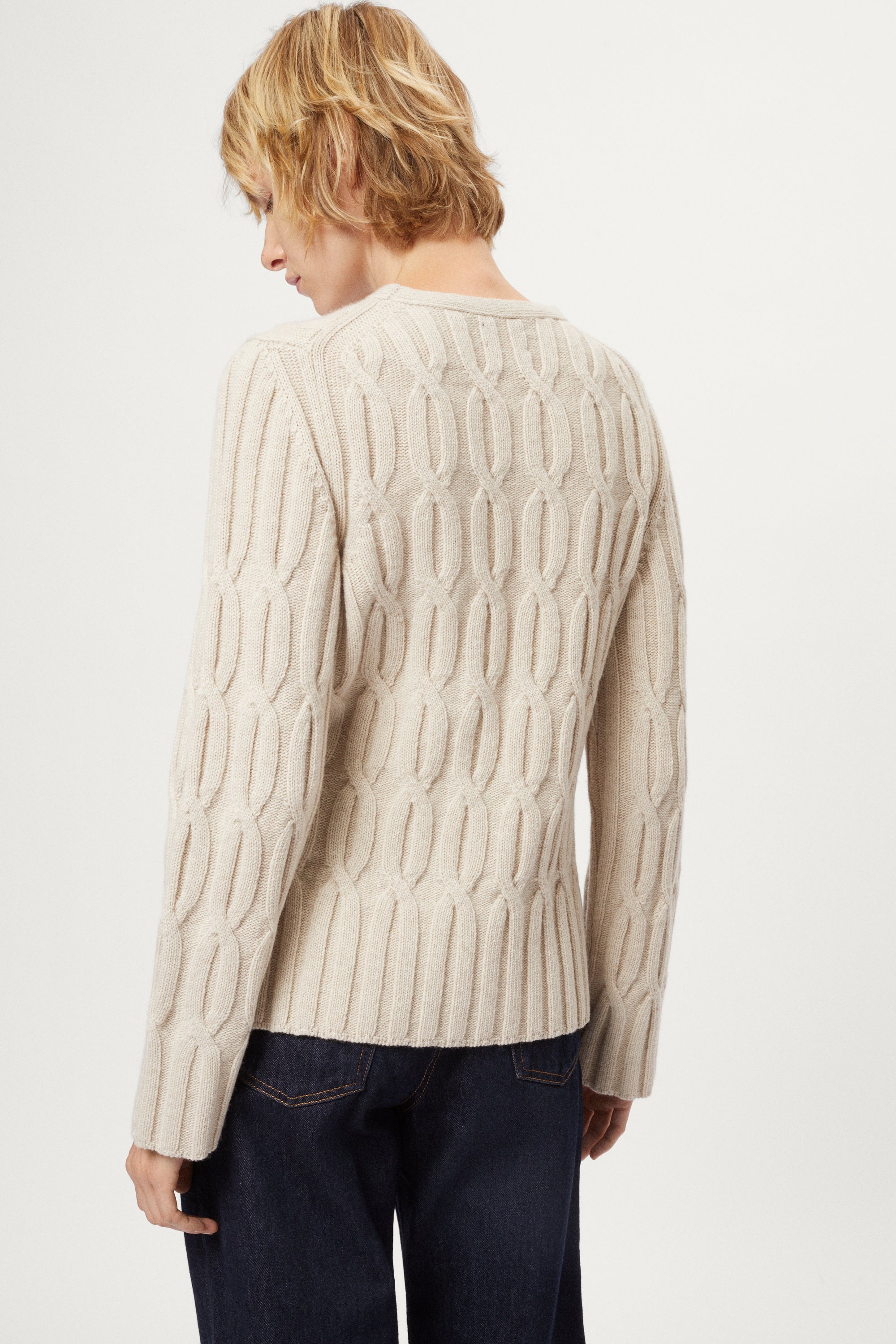Woman wearing an ecru woolen cable knit sweater and dark jeans on a white background