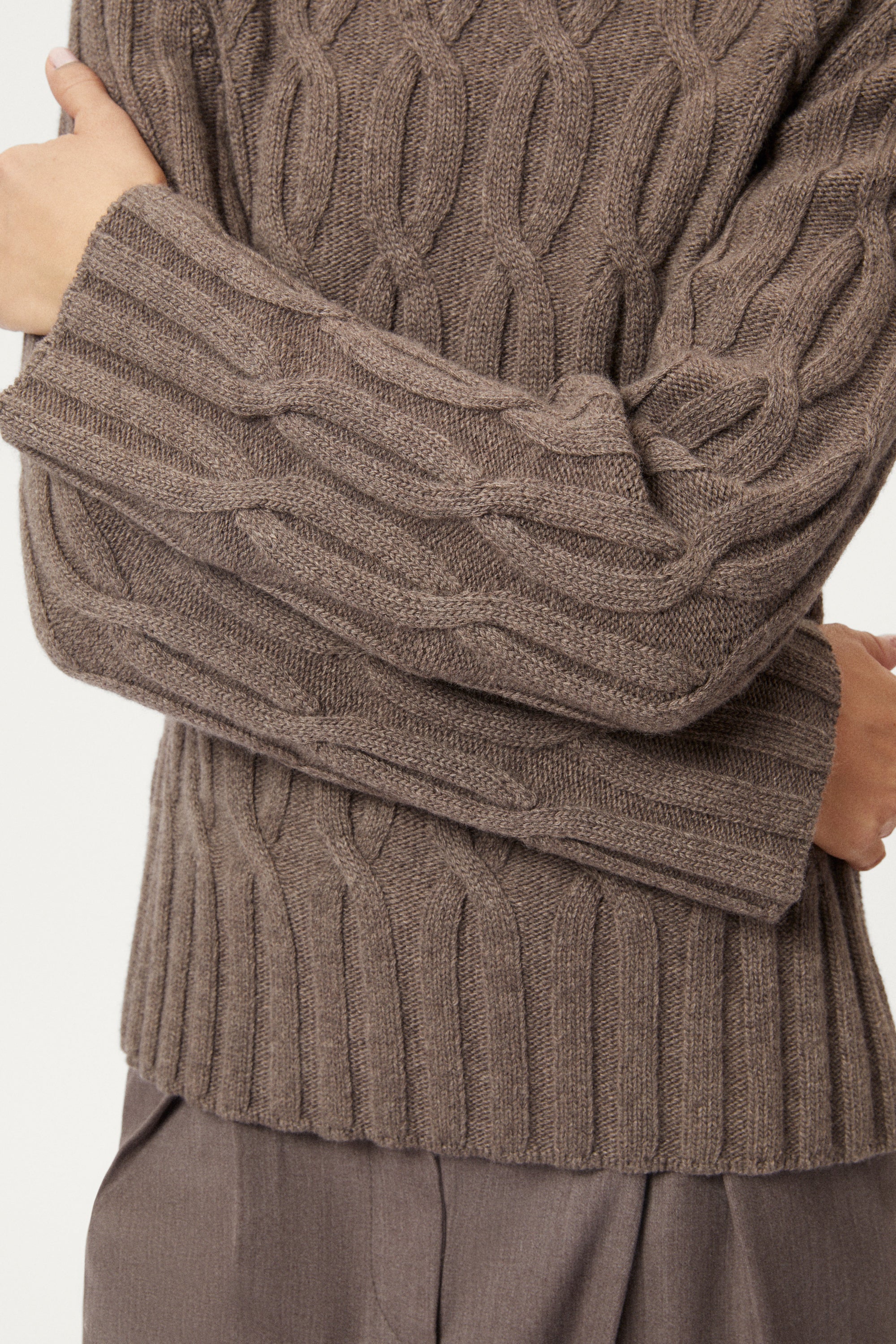 Close-up of a person wearing a brown cable knit sweater with a blurred background