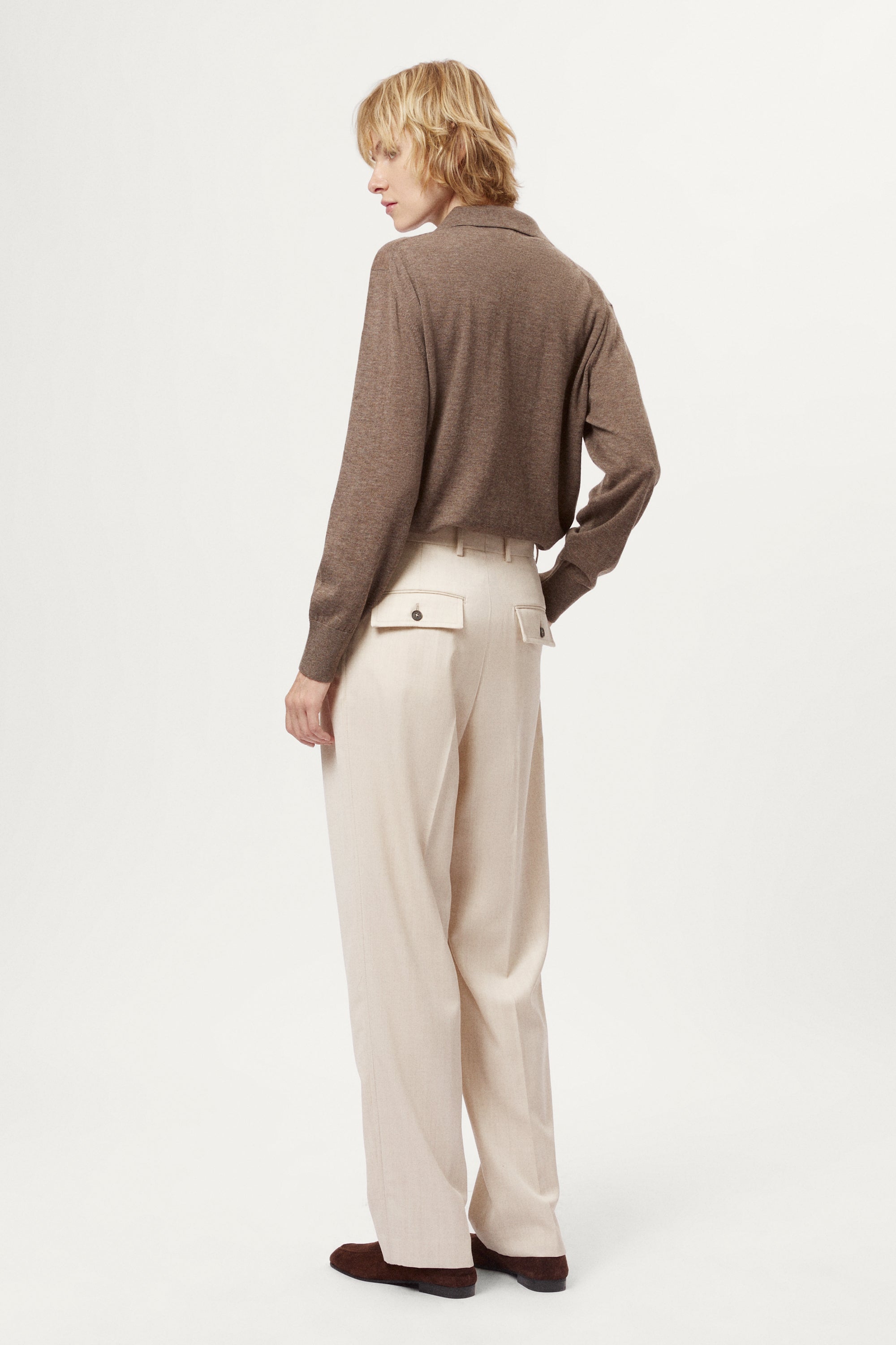 Person wearing a brown sweater and beige pants on a white background