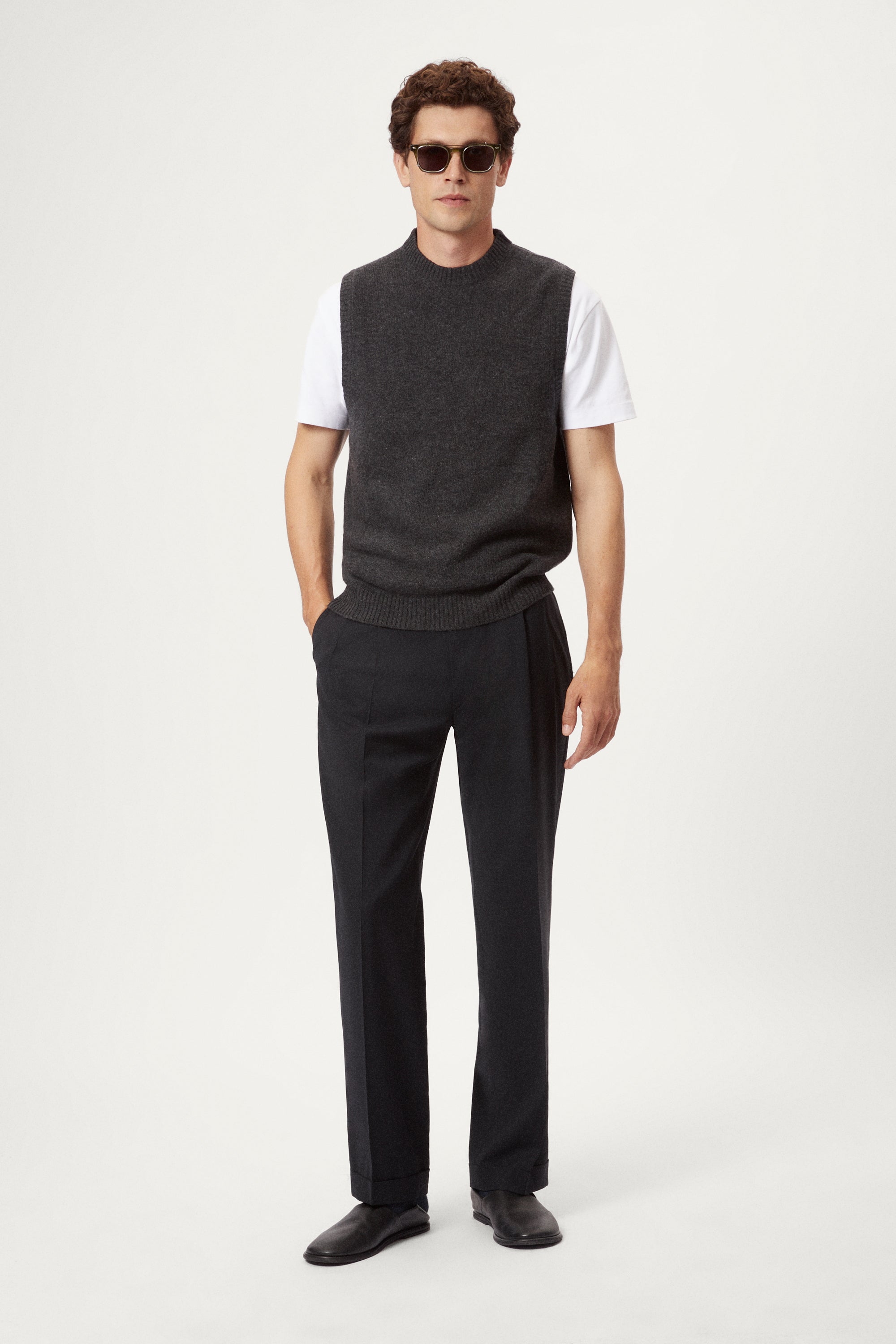 Man wearing a dark gray knitted vest over a white shirt on a light background