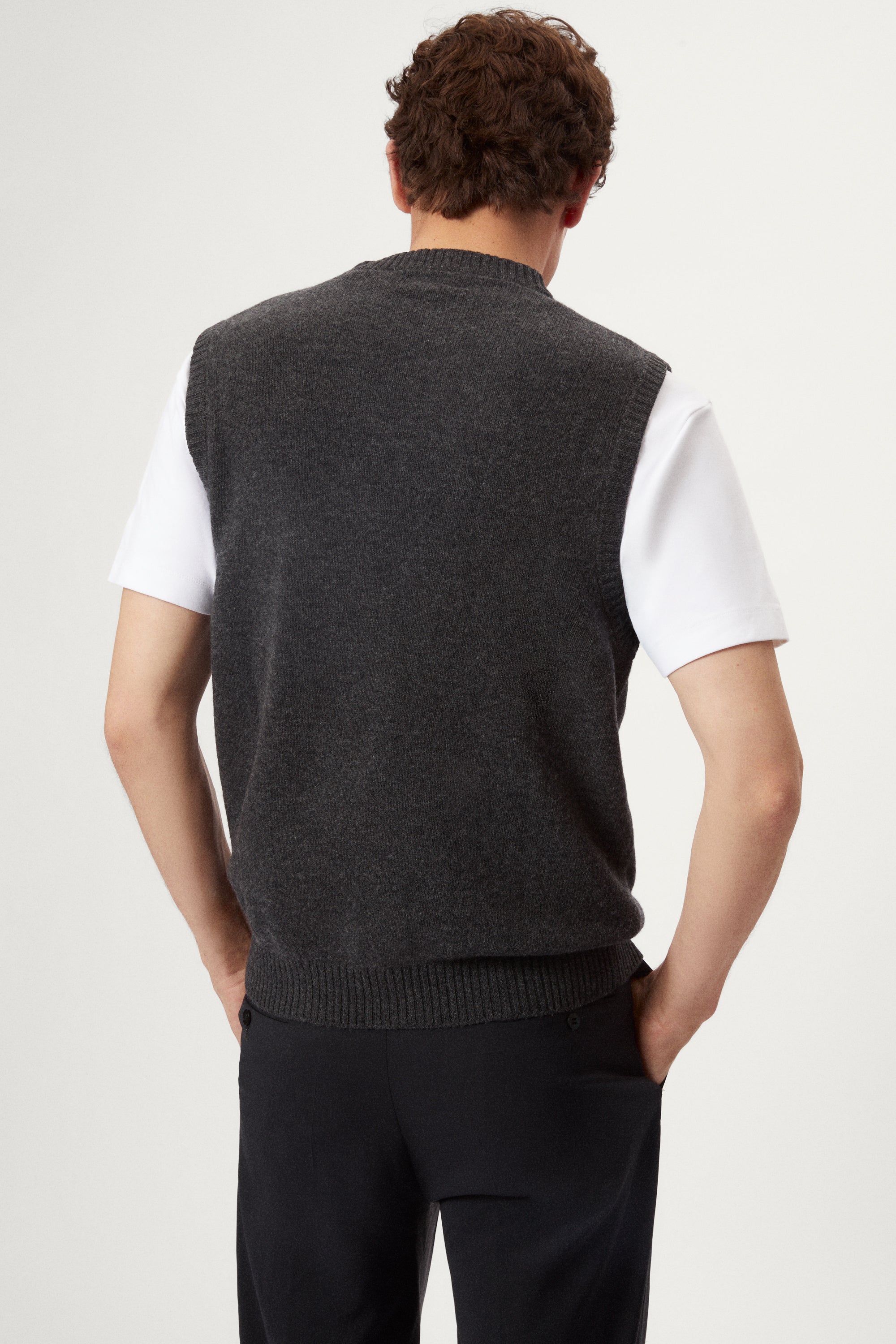 Man wearing a dark gray knitted vest over a white shirt on a light background