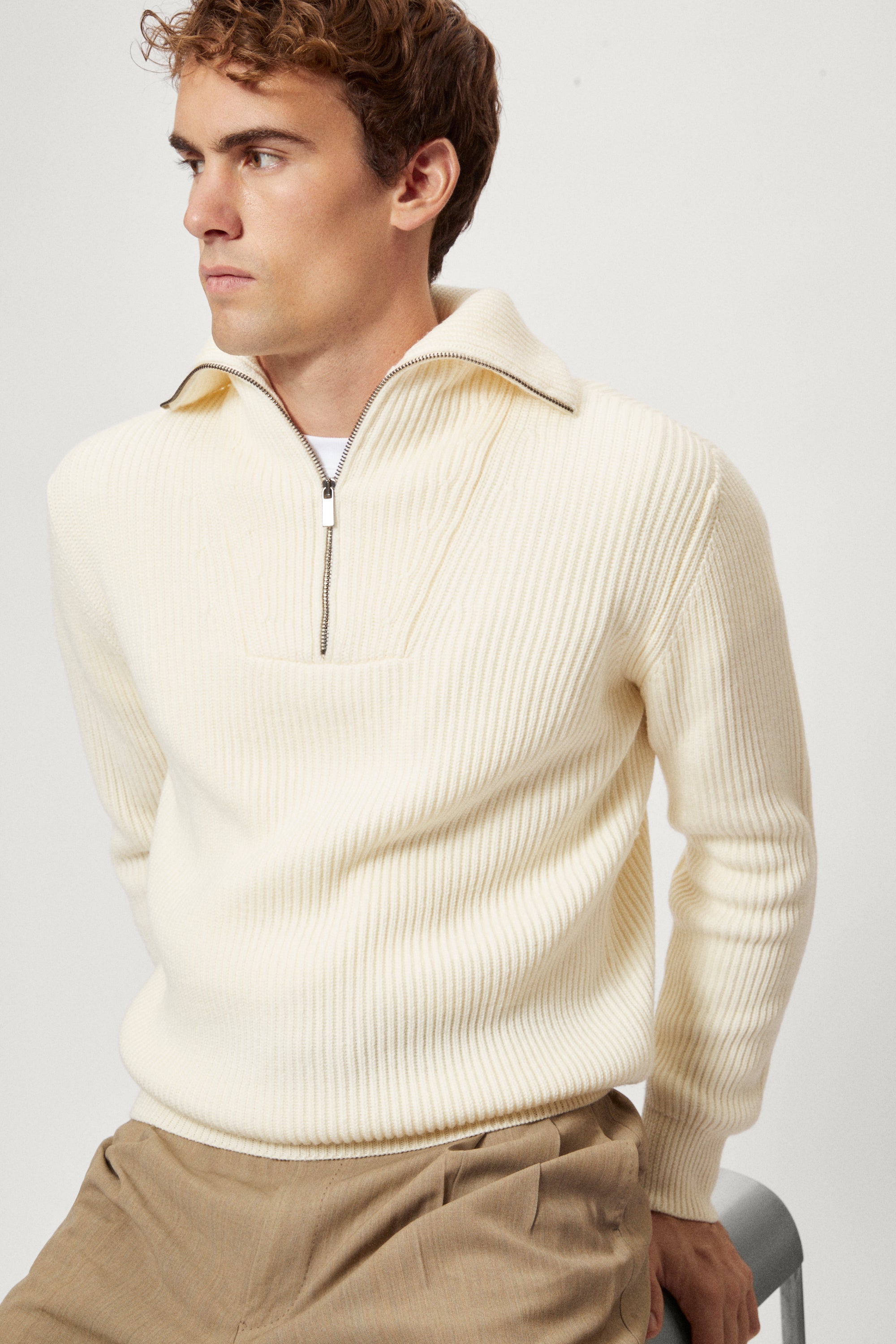 Man wearing a cream half-zip sweater against a white background