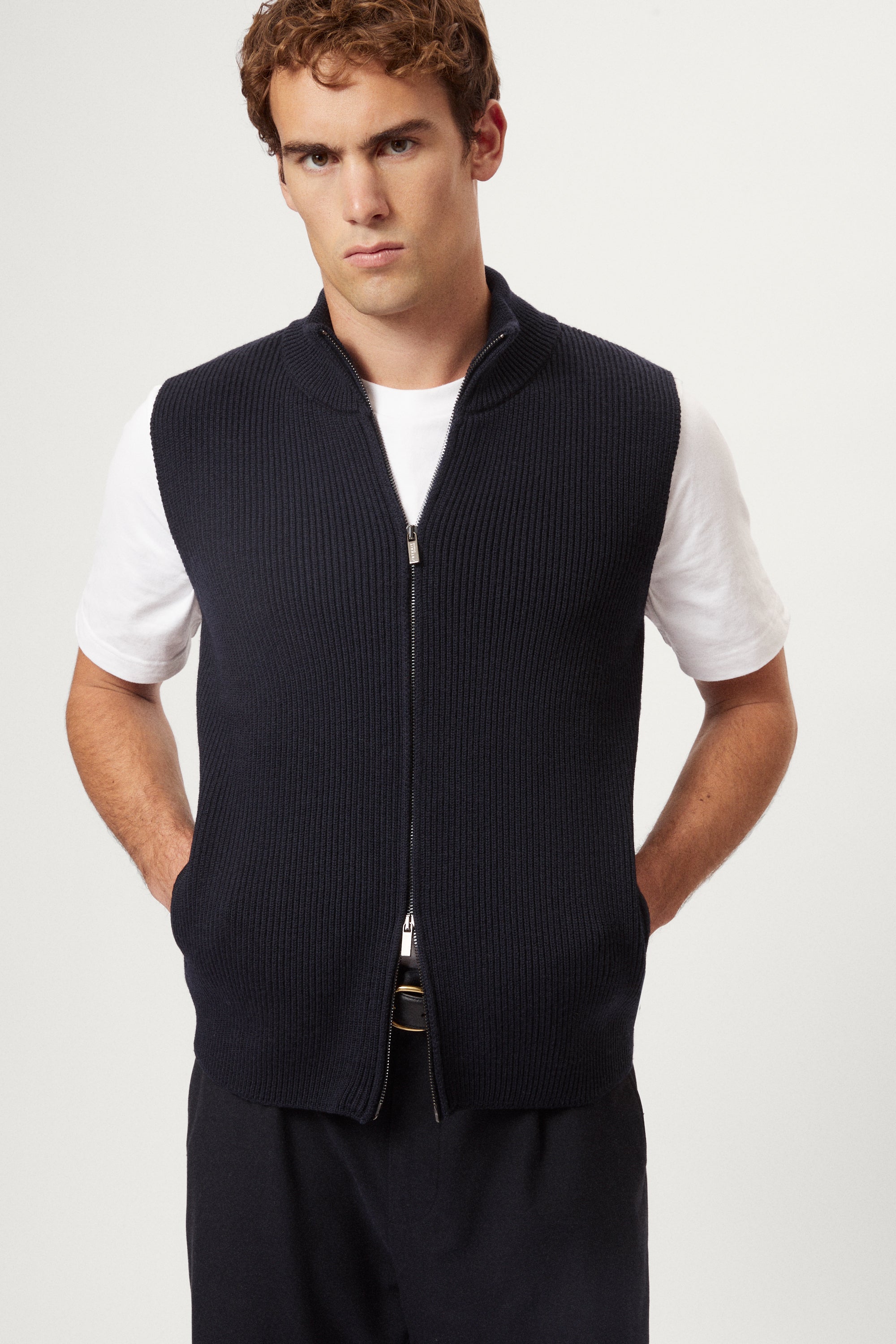 Man wearing a navy blue vest over a white shirt on a light gray background
