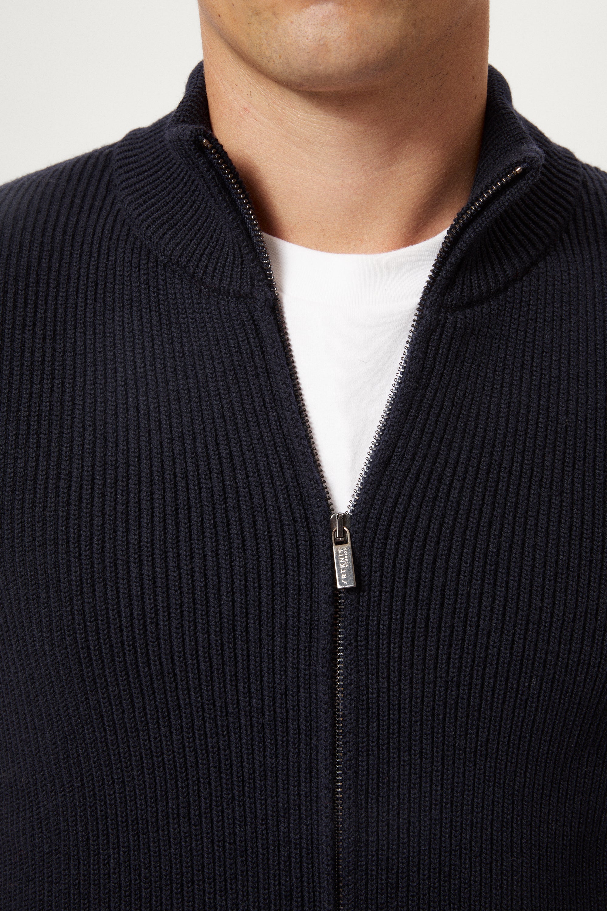 Close-up of a person a navy blue vest over a white shirt on a light gray background
