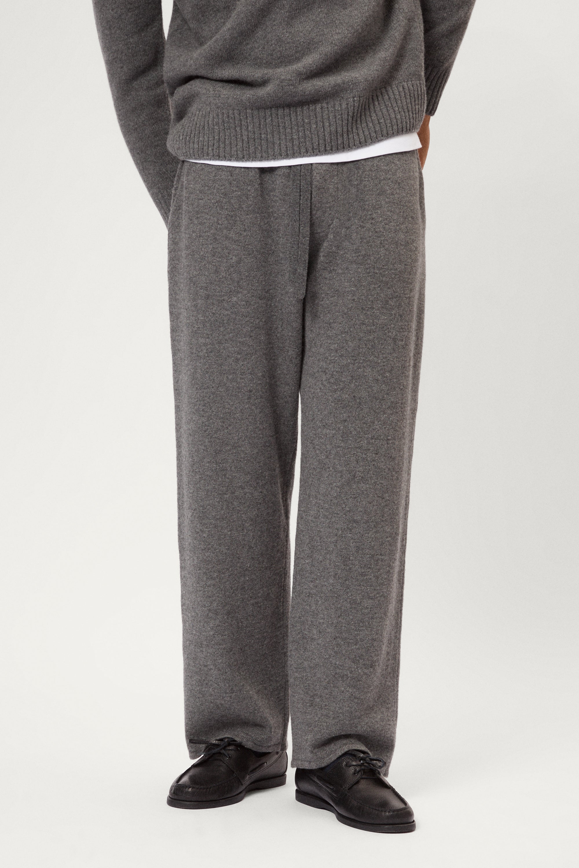 Person wearing a woolen gray knit pants and black shoes on a white background