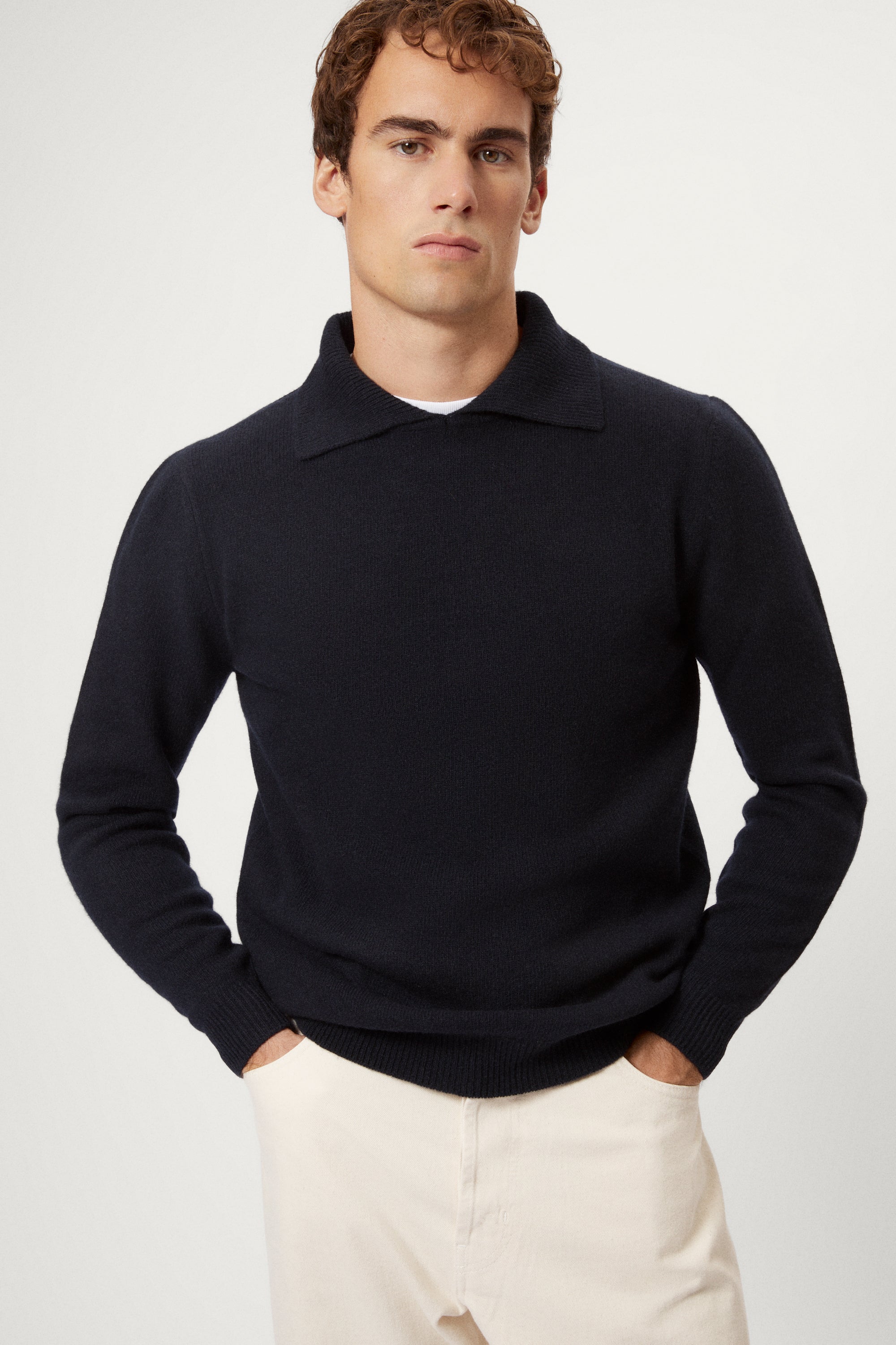 Man wearing a blue navy woolen polo sweater with a white background