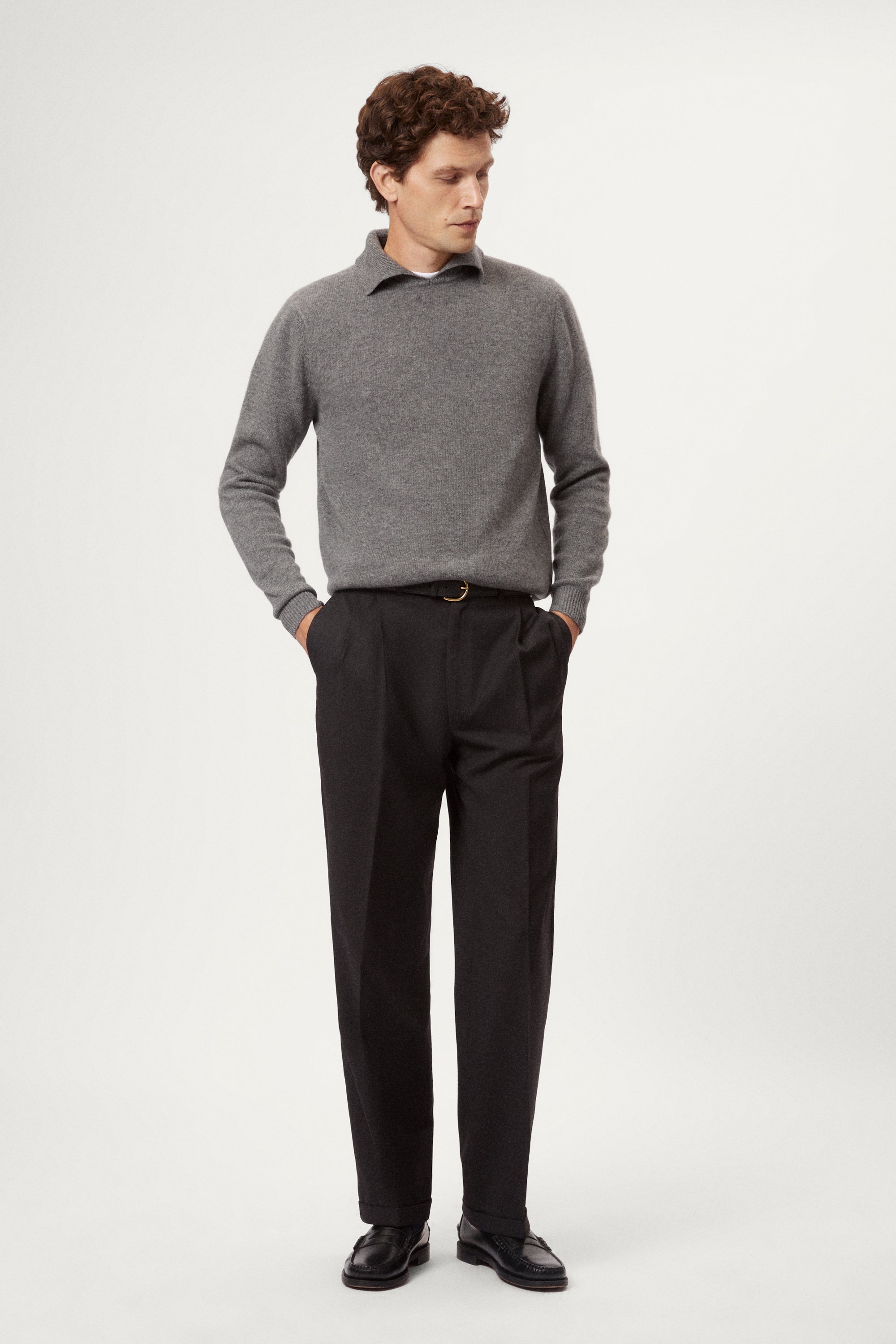 Man wearing a gray woolen  polo sweater and black pants on a white background