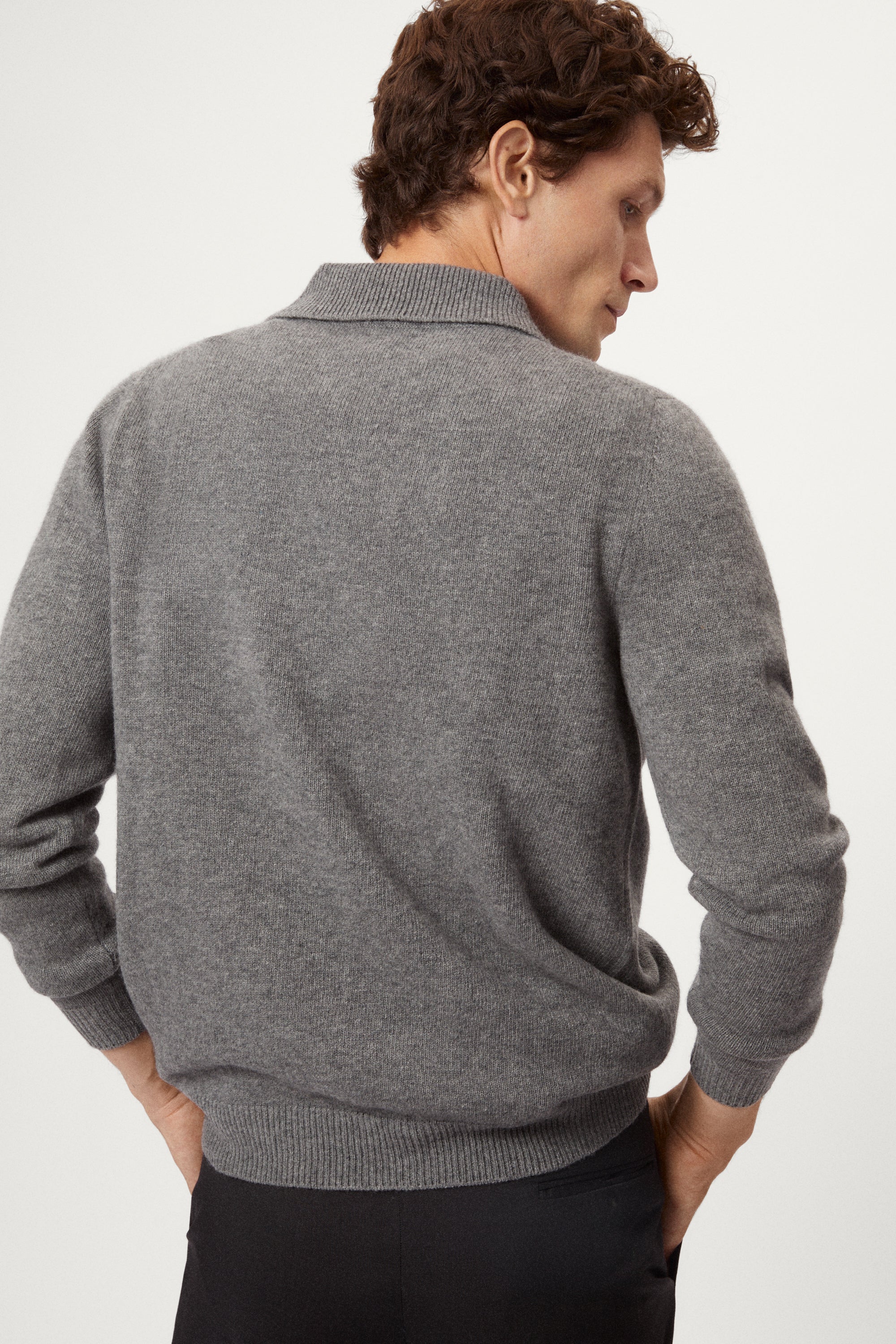 Man wearing a gray woolen  polo sweater and black pants on a white background