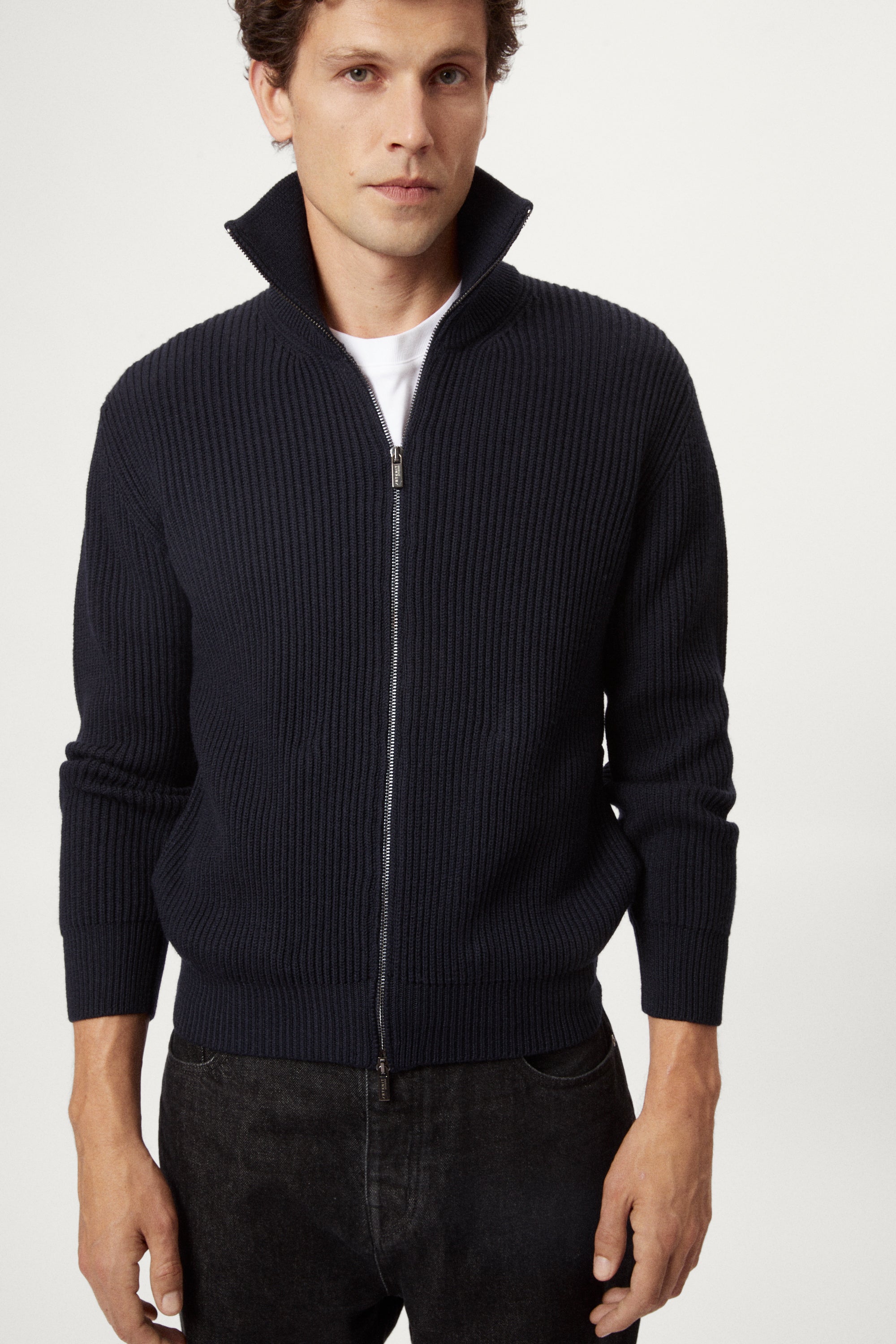 Man wearing a dark blue zip-up sweater over a white shirt on a white background