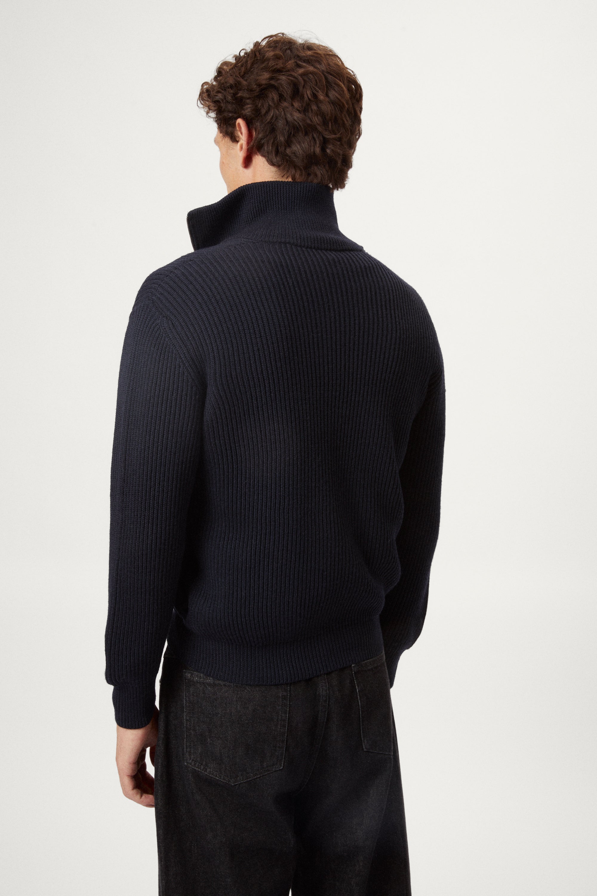 Man wearing a dark blue zip-up sweater over a white shirt on a light gray background