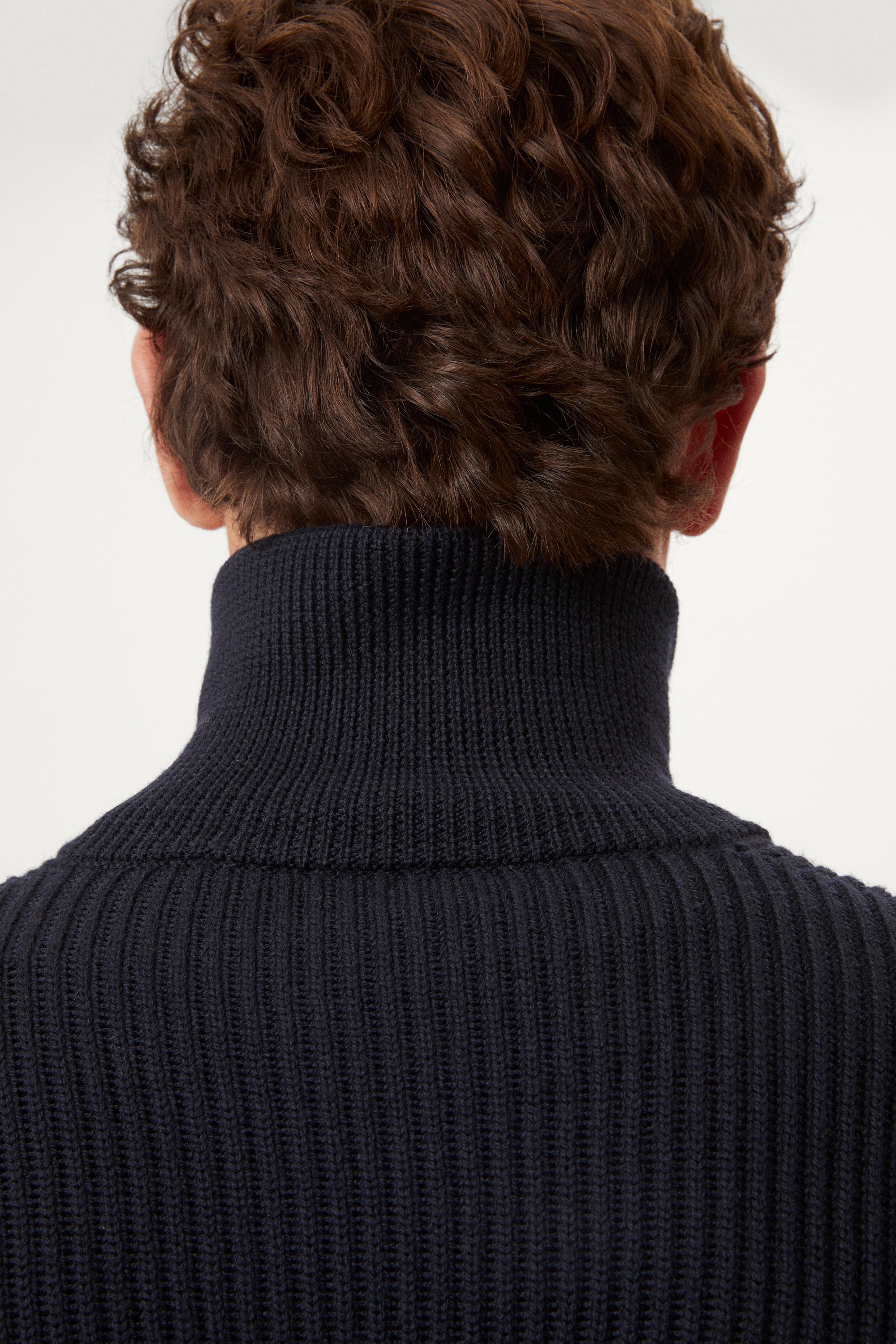 Man wearing a dark blue zip-up sweater over a white shirt on a light gray background