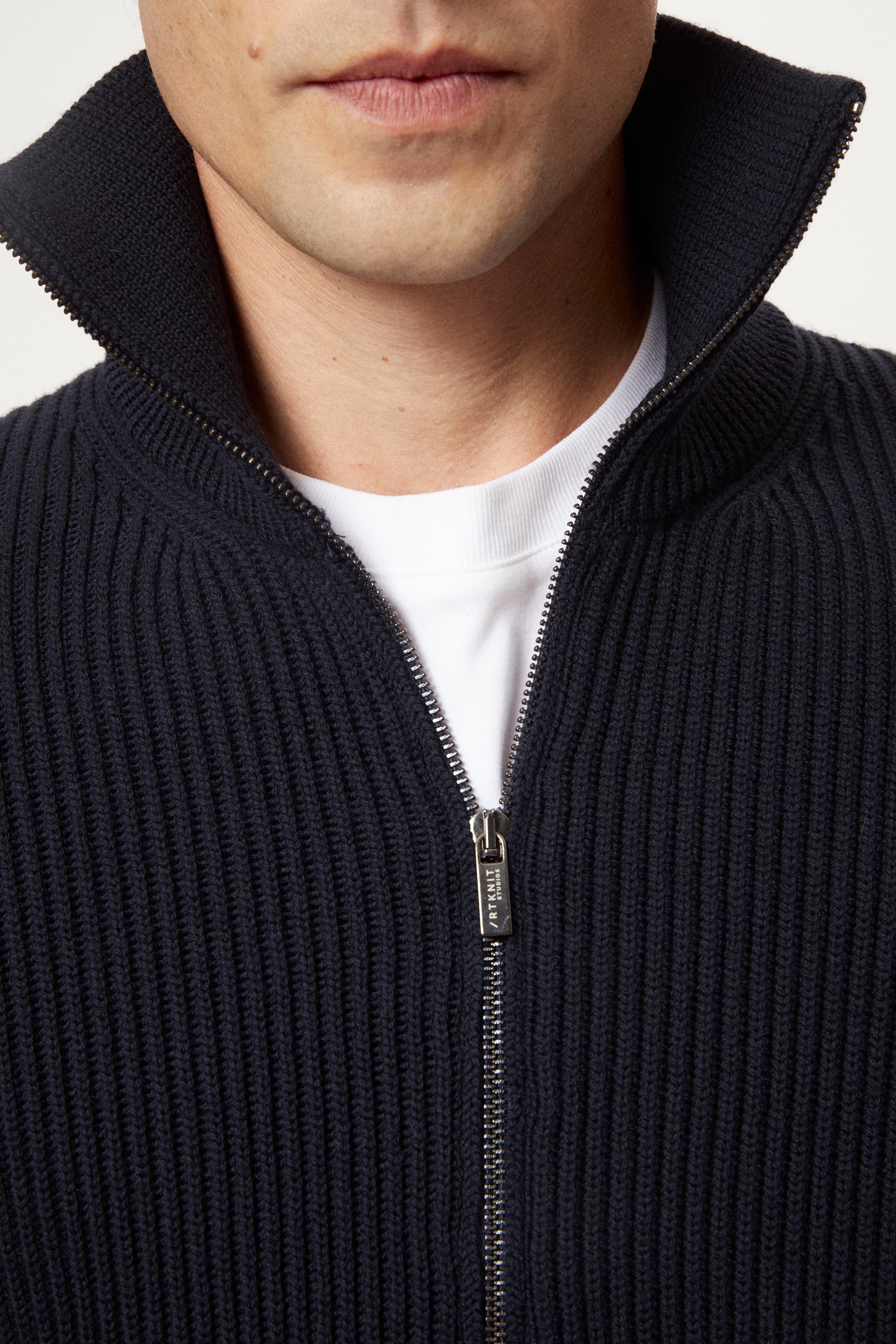 Man wearing a dark blue zip-up sweater over a white shirt on a light gray background