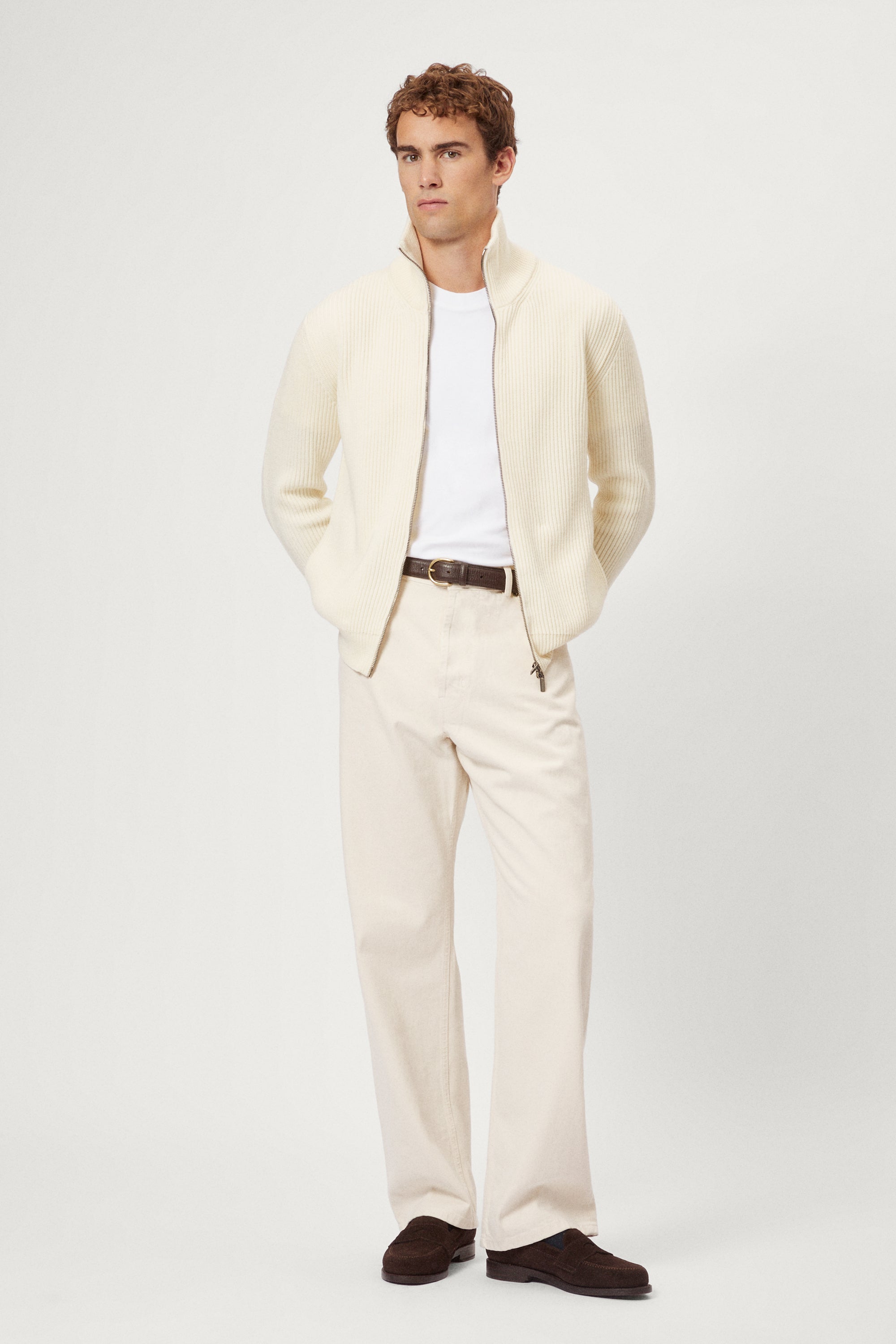 Man wearing a cream suit with a white shirt and brown shoes on a white background