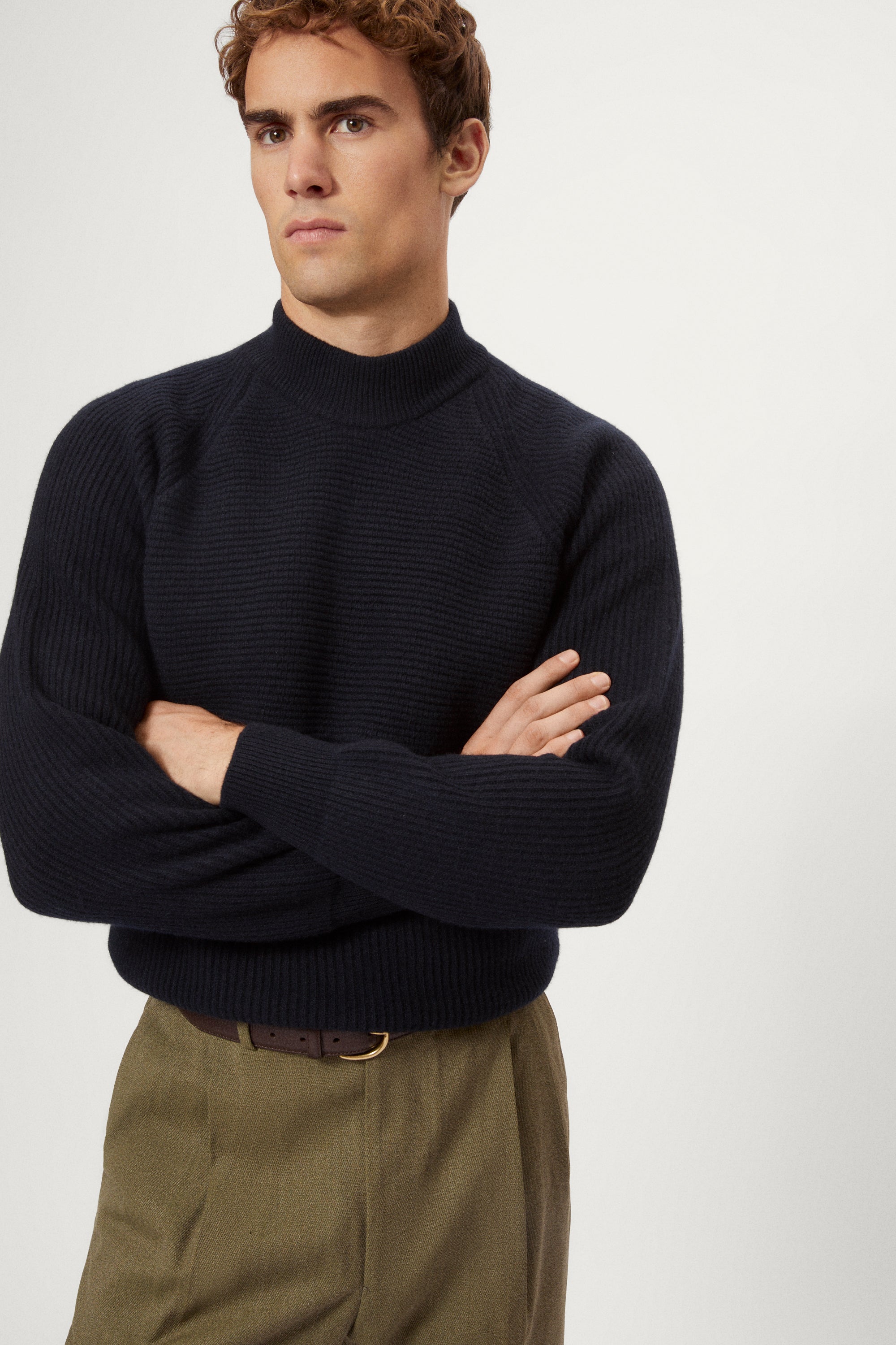 Man wearing a dark blue woolen sweater and green pants on a white background