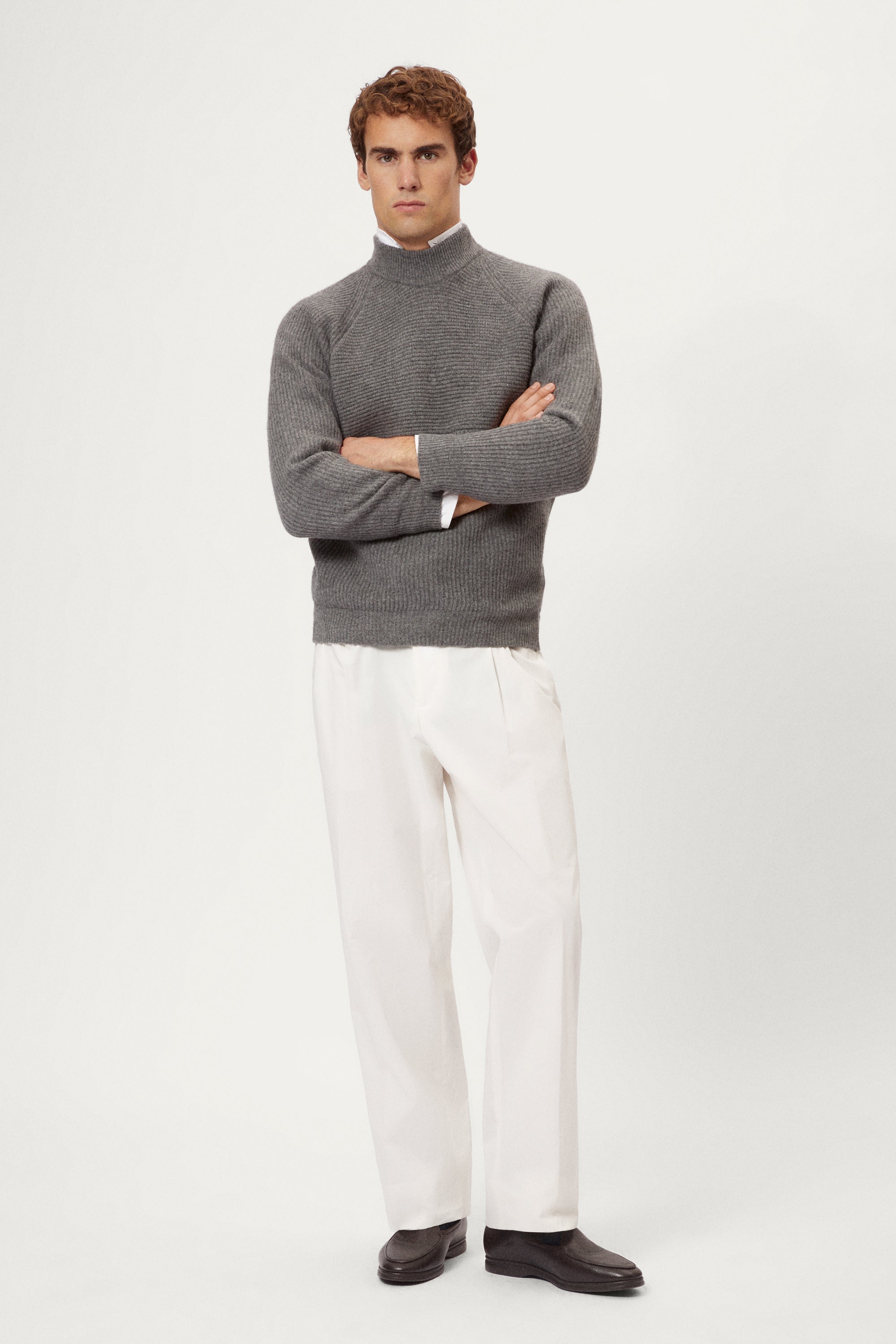 Man wearing a gray  ribbed sweater and white pants on a light background