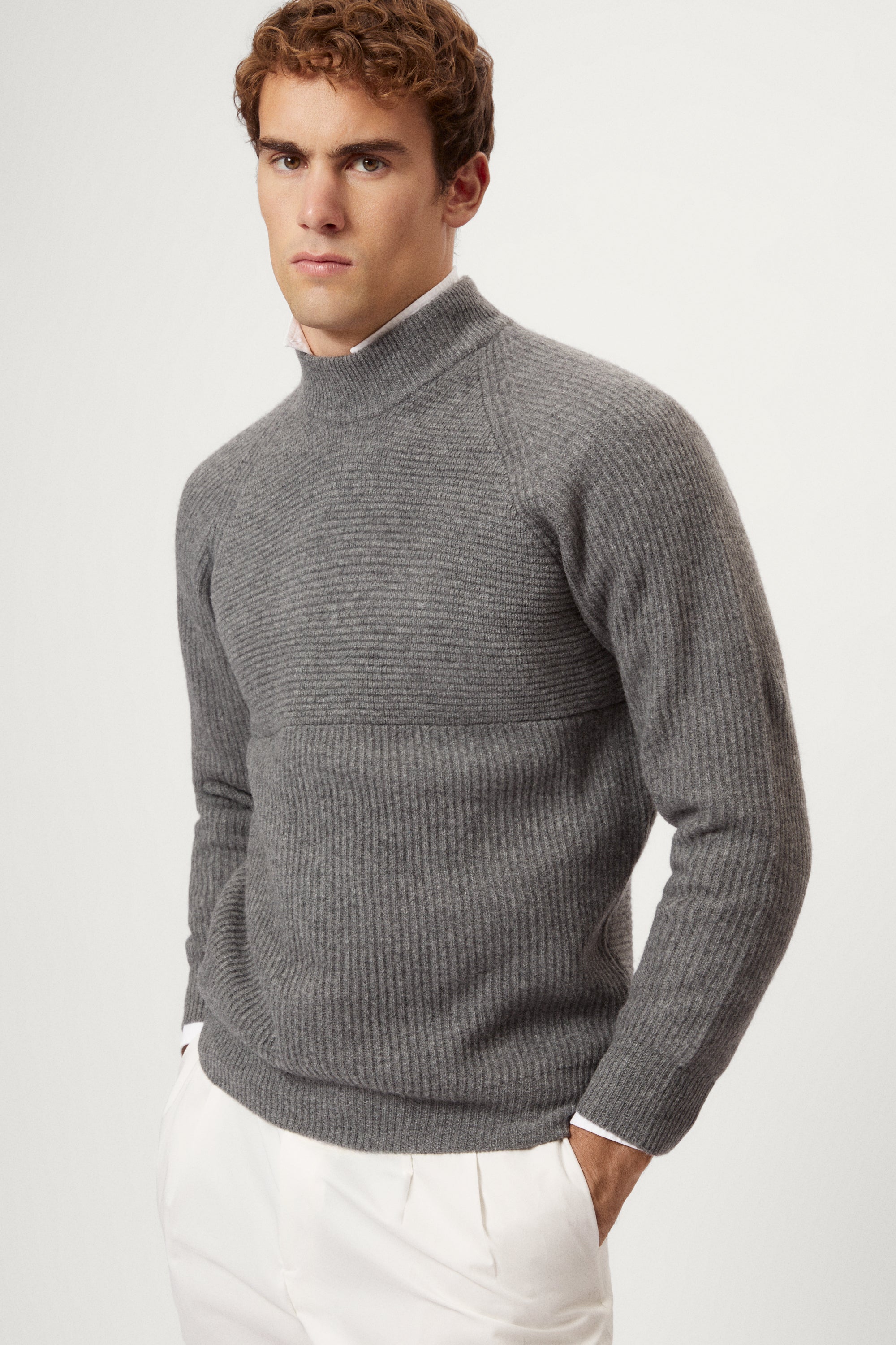 Man wearing a gray  ribbed sweater and white pants on a light background
