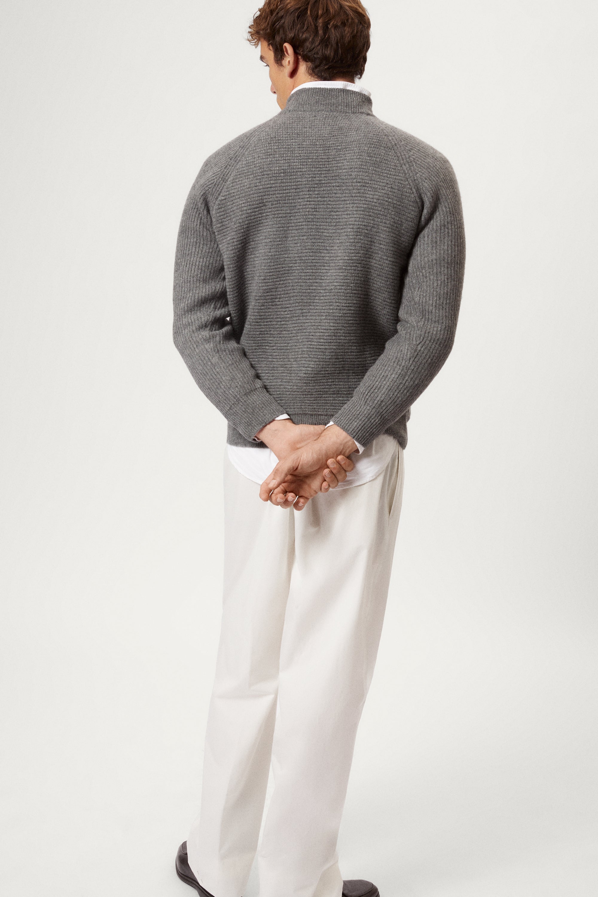 Man wearing a gray  ribbed sweater and white pants on a light background