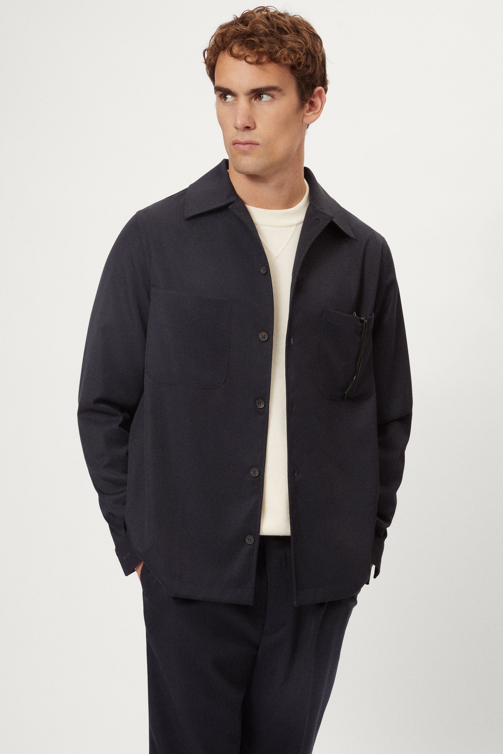 Man wearing a dark jacket over a white shirt on a light gray background