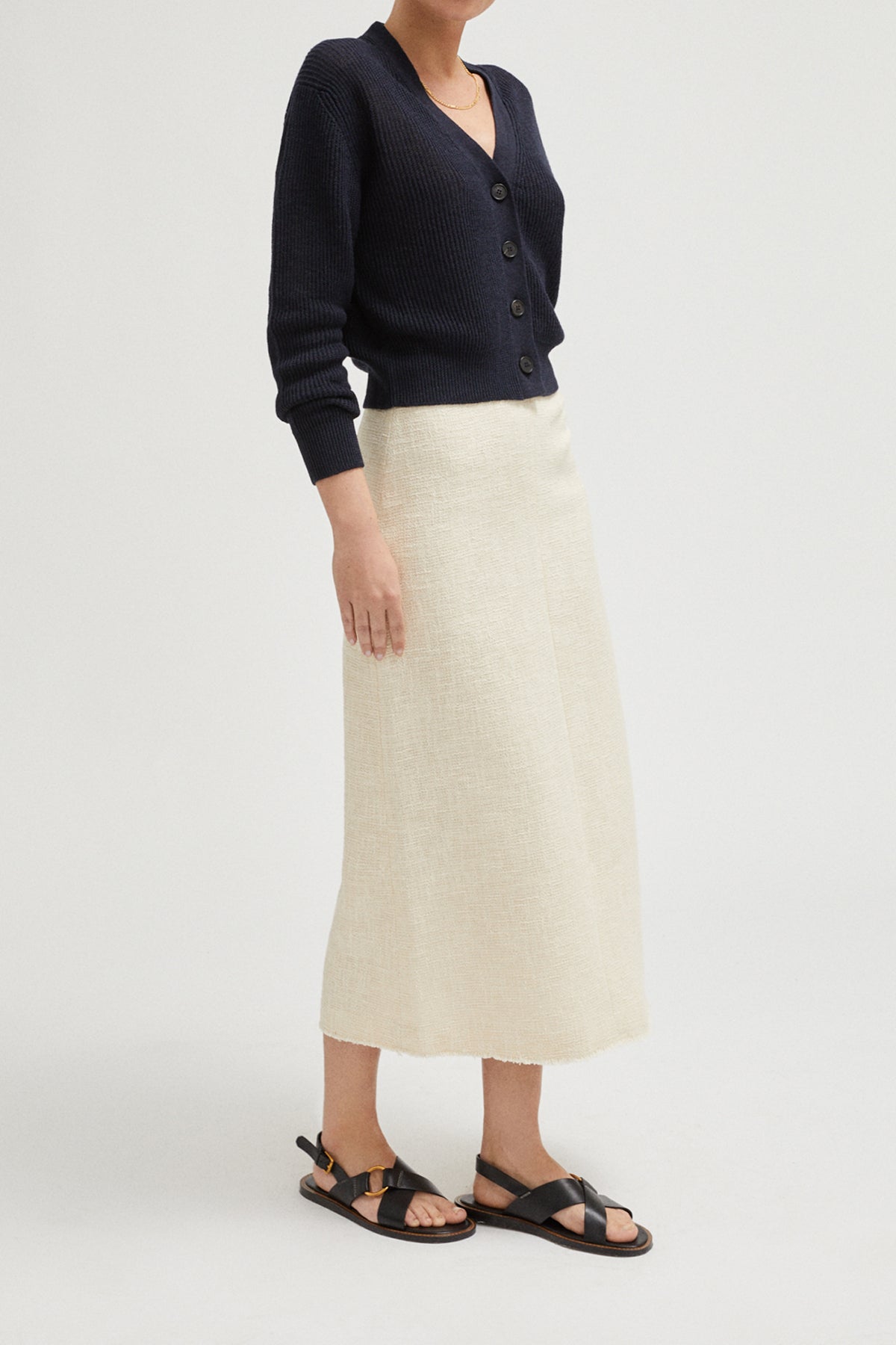 Person wearing a navy cardigan, white skirt, and black sandals on a light gray background