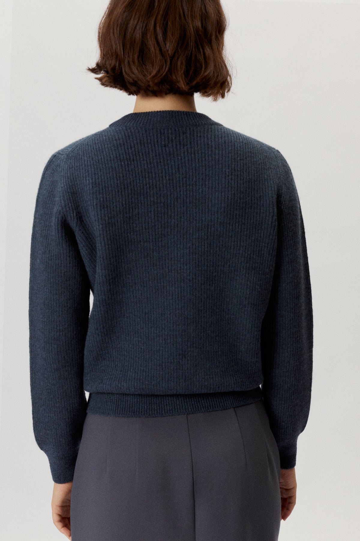 Person wearing a dark blue sweater and gray pants on a light gray background