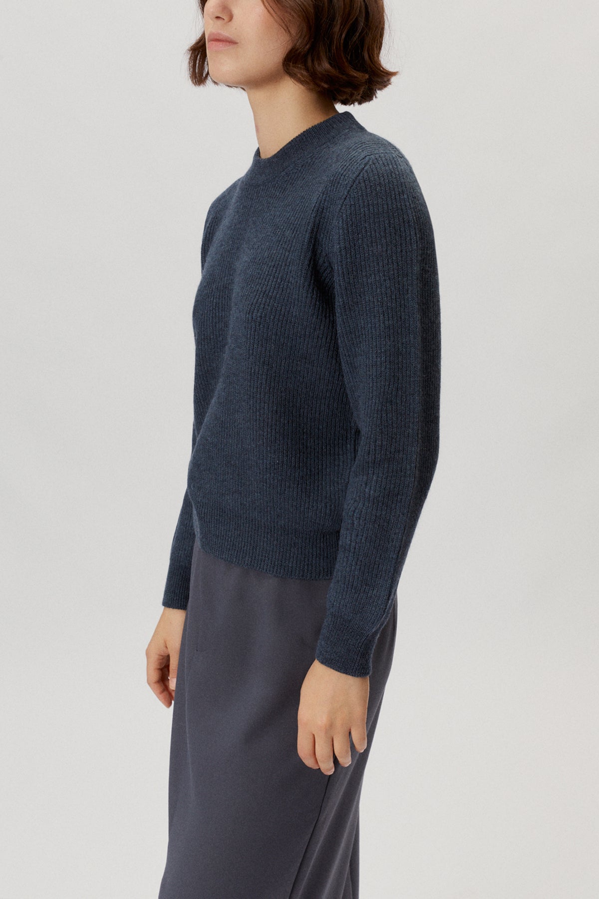 Person wearing a dark blue sweater and gray skirt on a light gray background