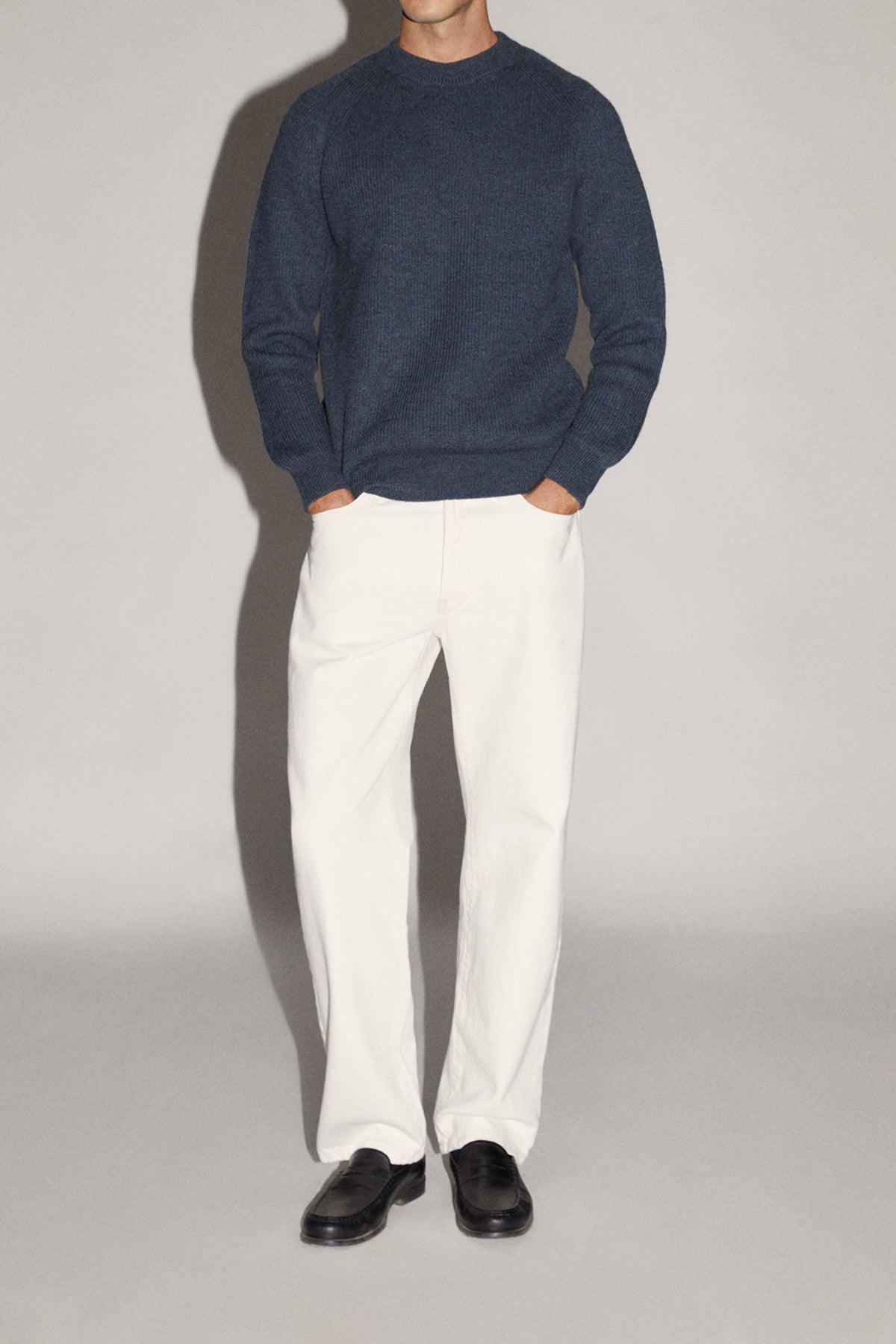 Person wearing a navy sweater and white pants on a plain background