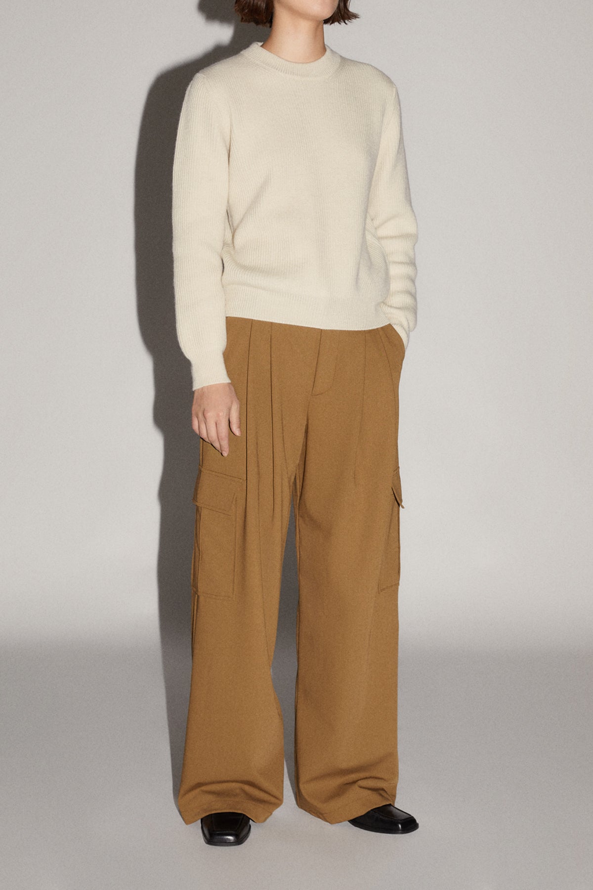 Person wearing a beige sweater and brown pants on a plain background