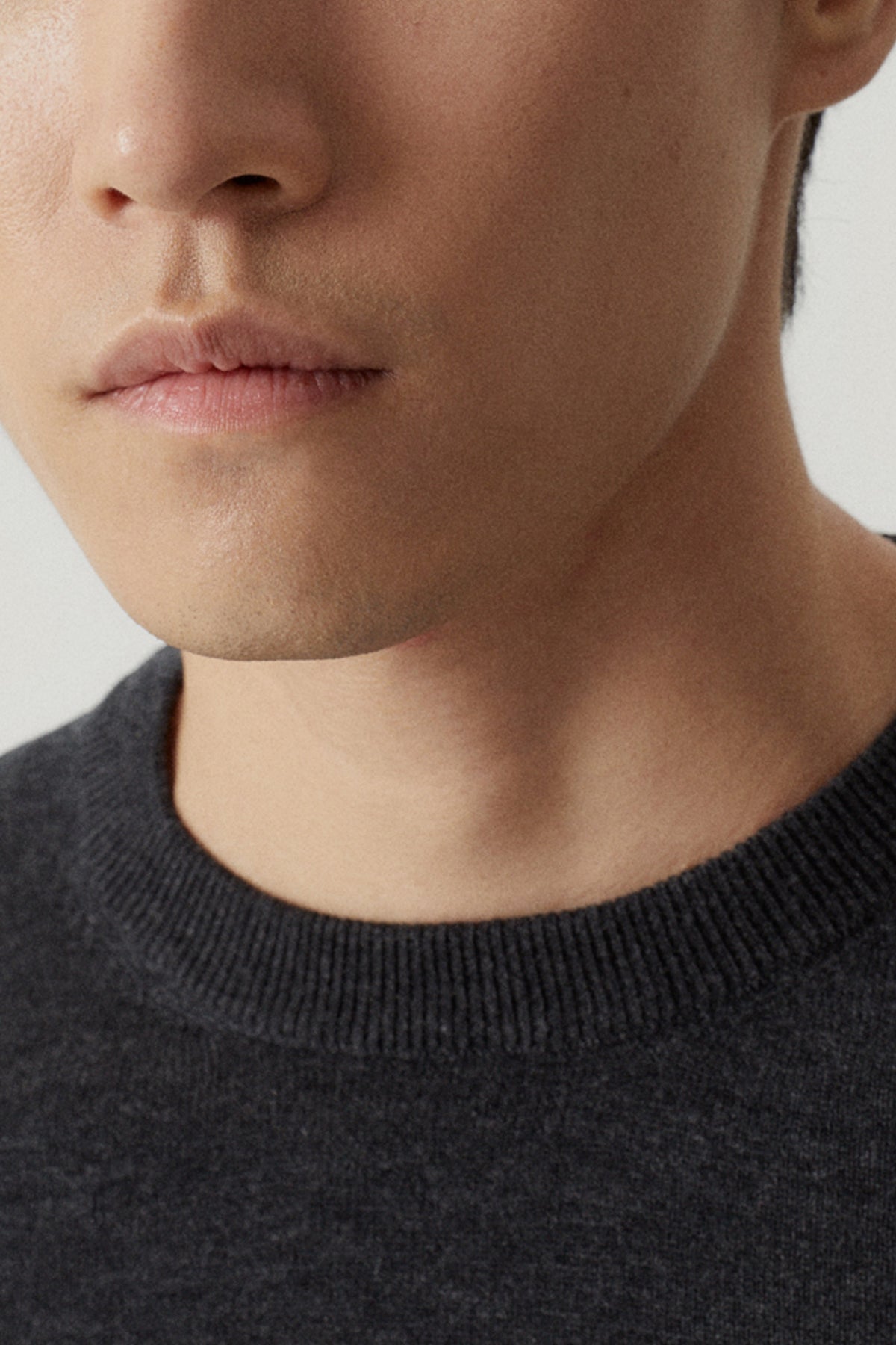 Close-up of a person wearing a dark gray sweater against a neutral background